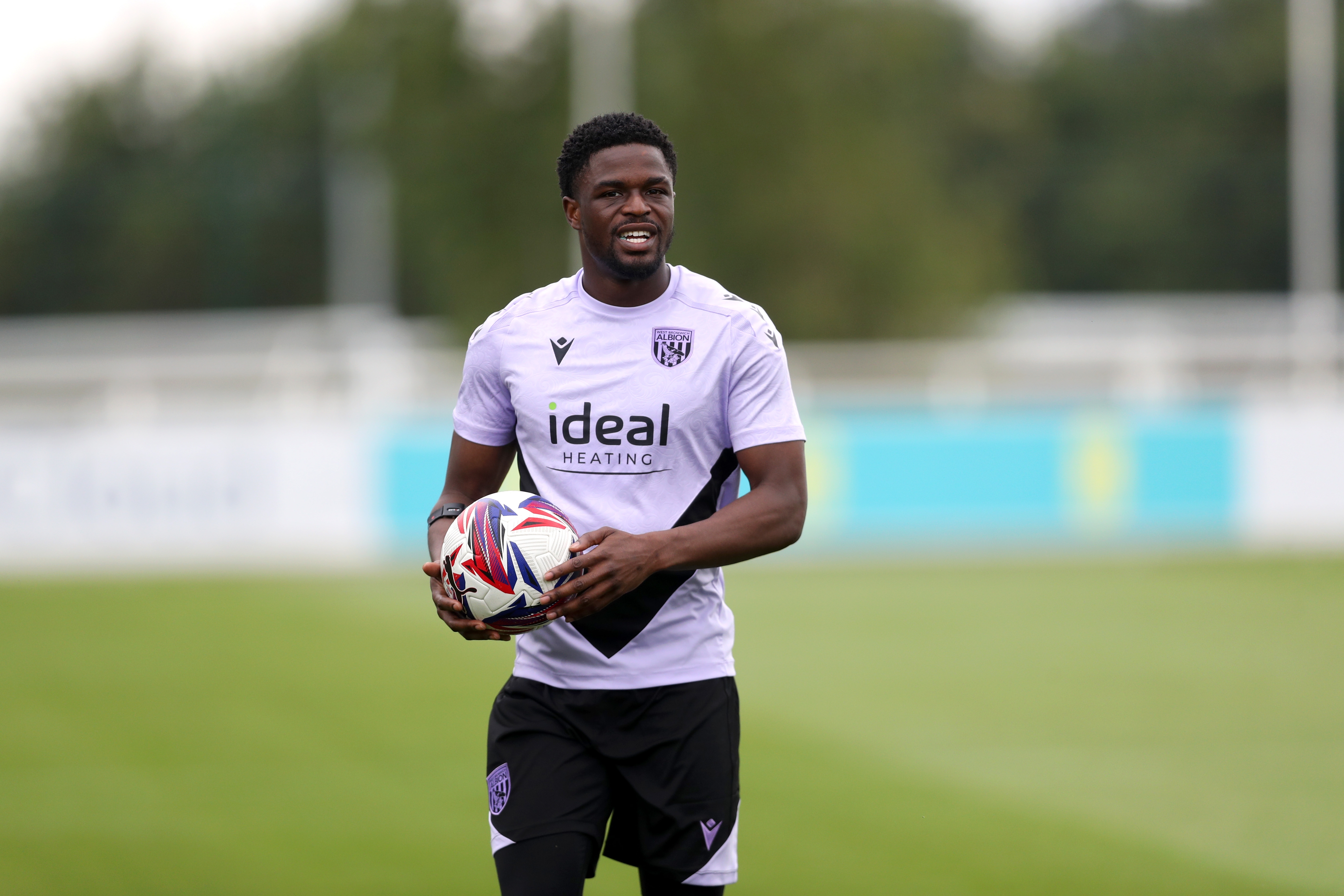 Josh Maja smiling and holding a ball on the training pitch at St. George's Park