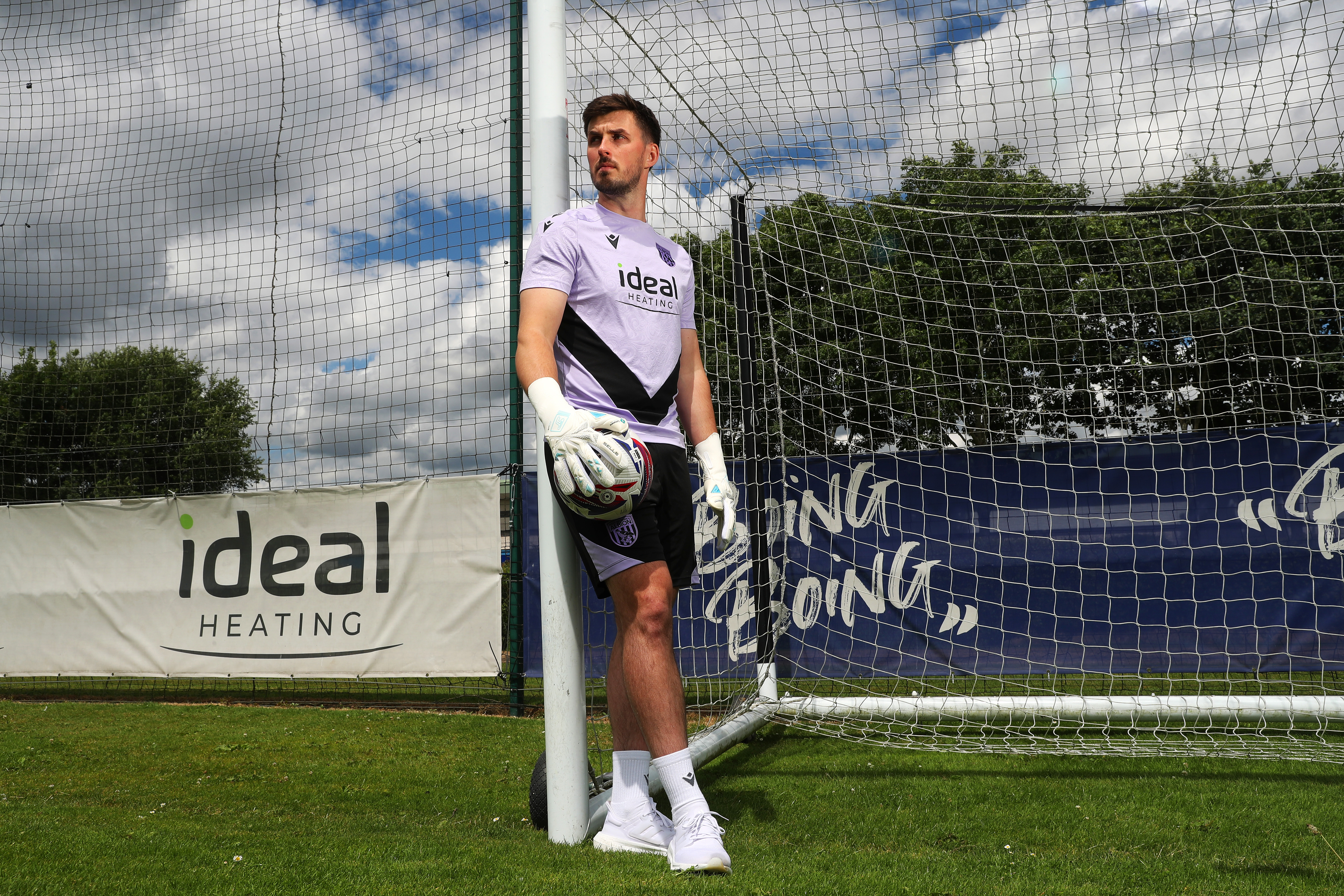 Joe Wildsmith stood up against a goal post holding a football looking away from camera