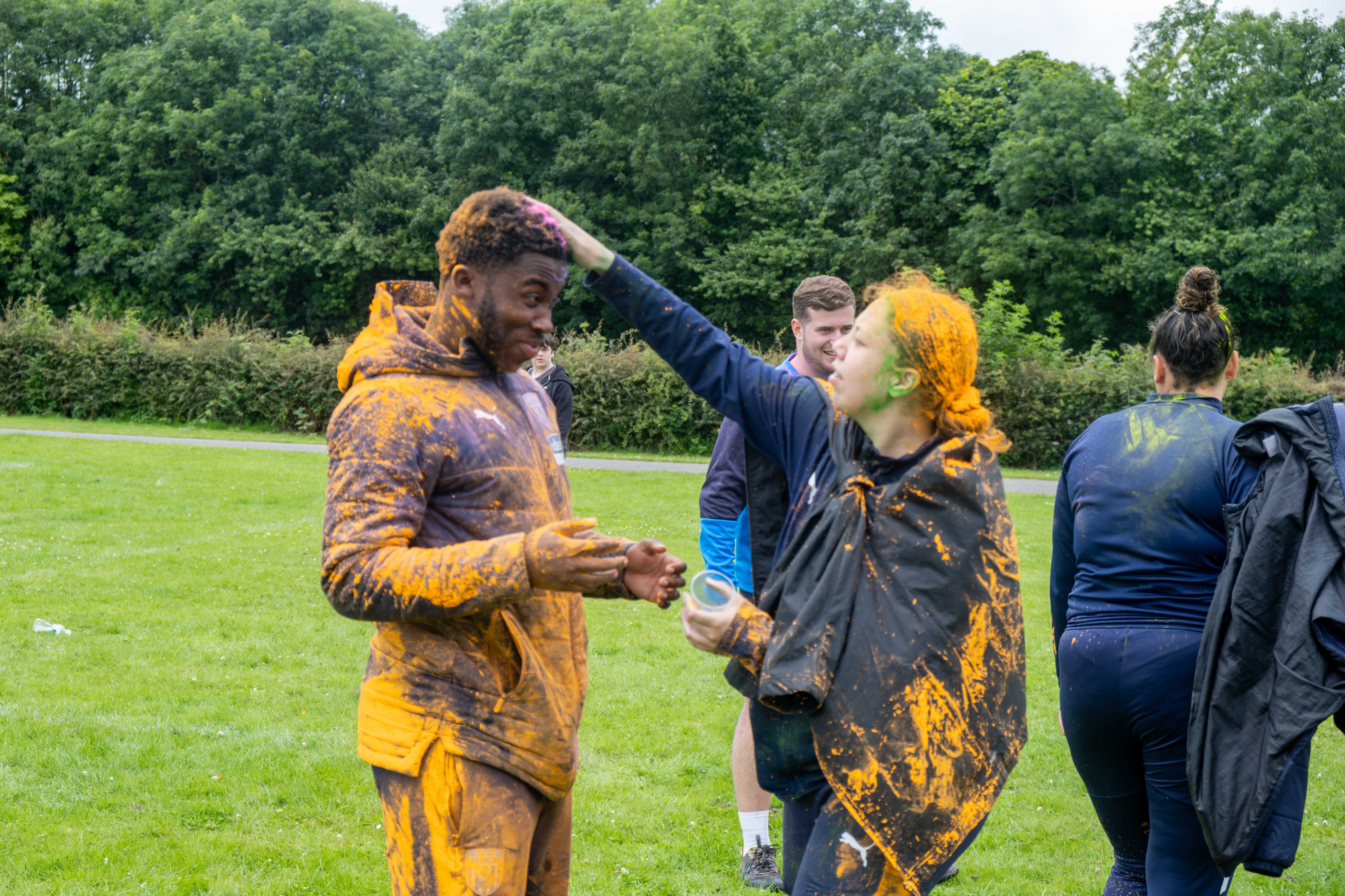 Two Foundation staff members covering each other with orange paint powder