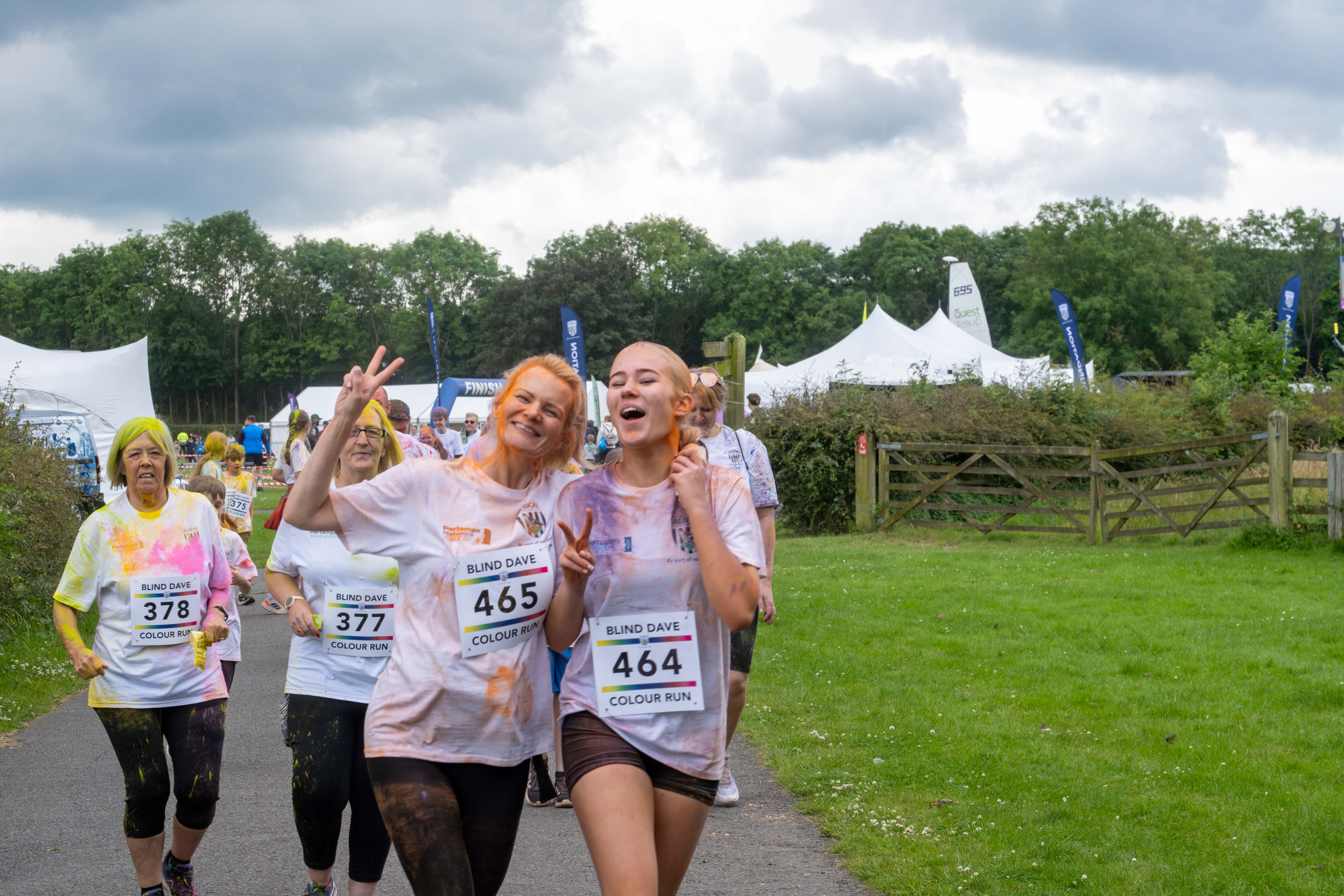 Two participants running with arms around each other. One showing peace sign, with other runners behind them.