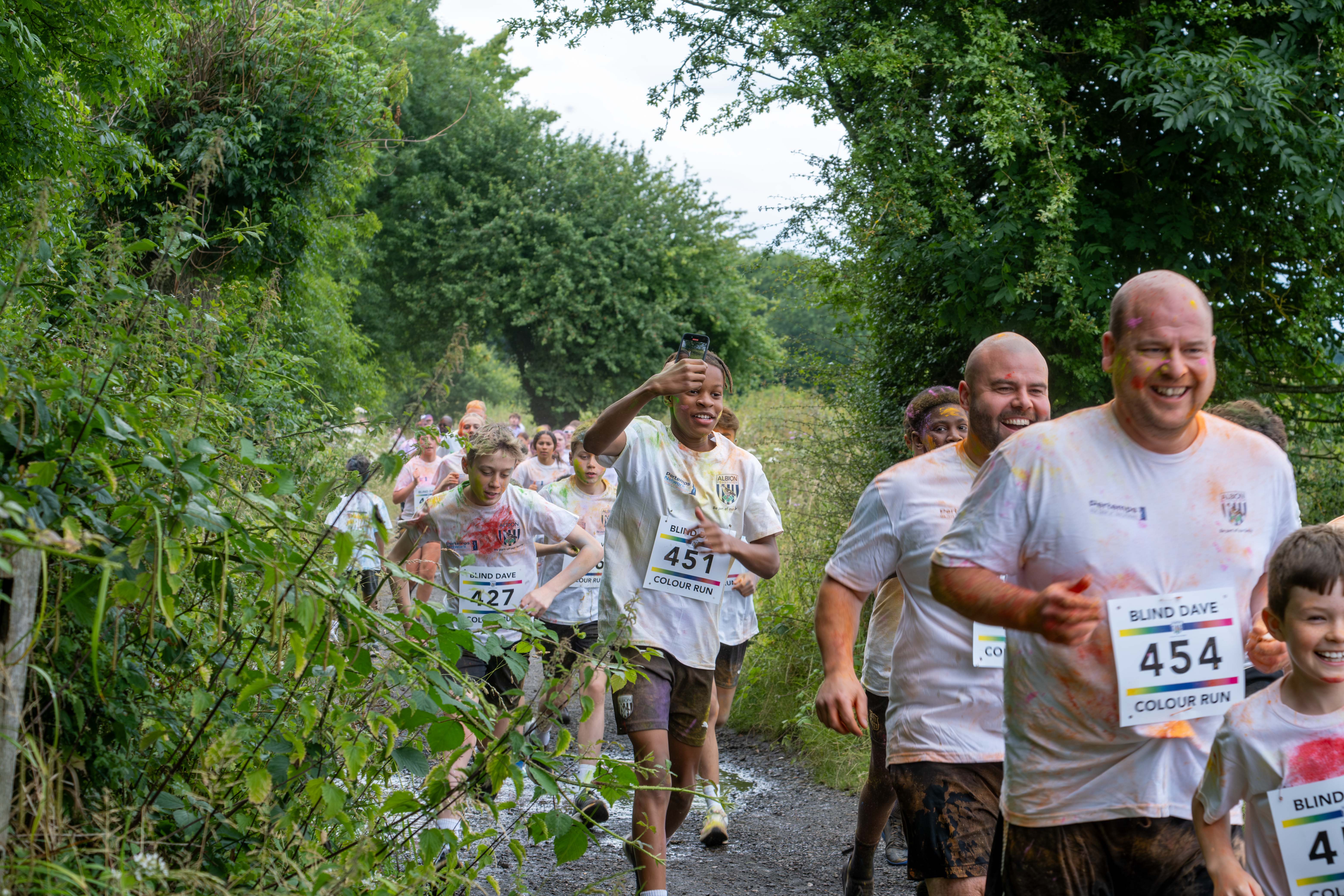 Runners heading through shrubs on Sandwell Valley Park. One participant recording on his phone.