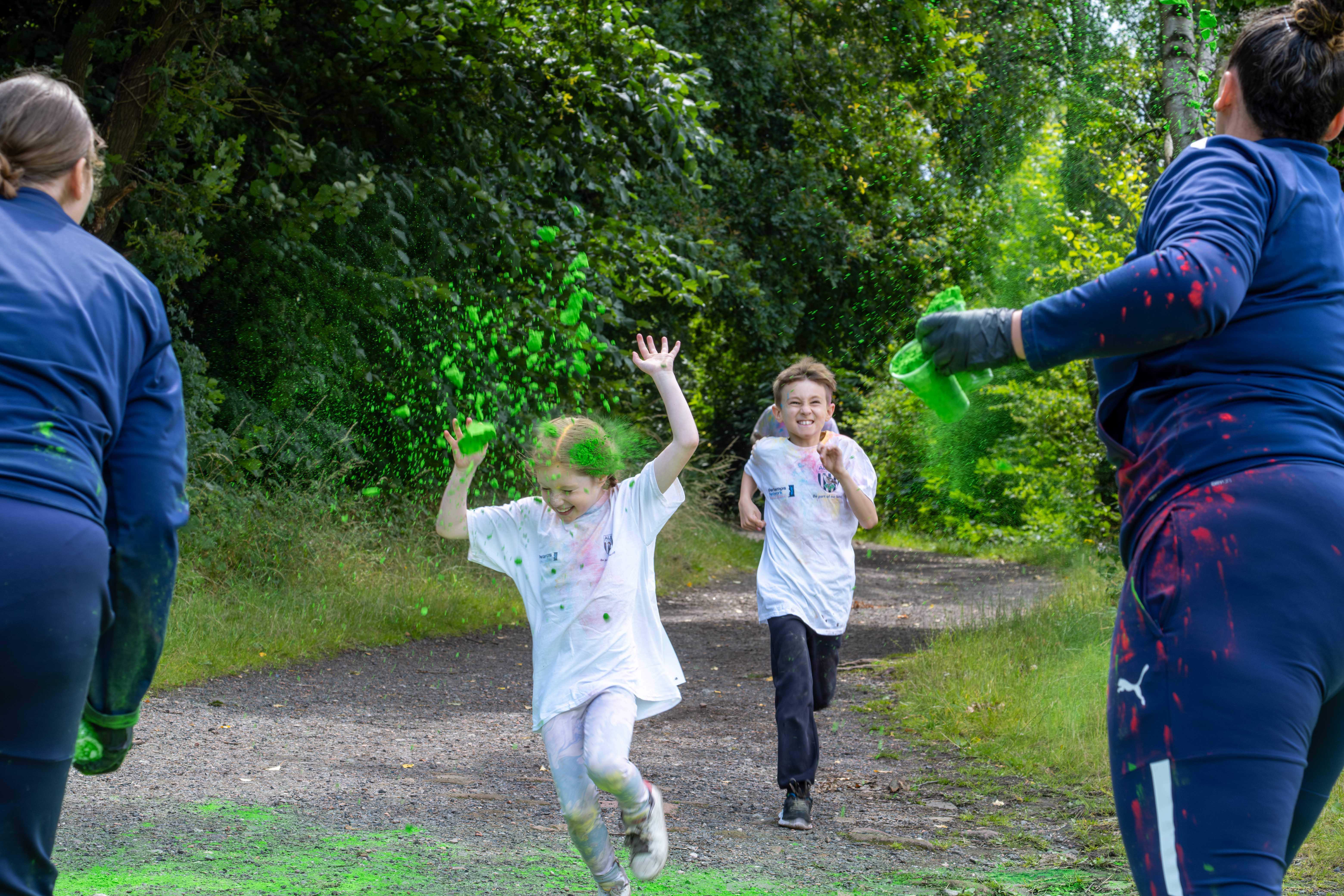 Two young participants running towards Foundation staff at a colour station, throwing paint powder.