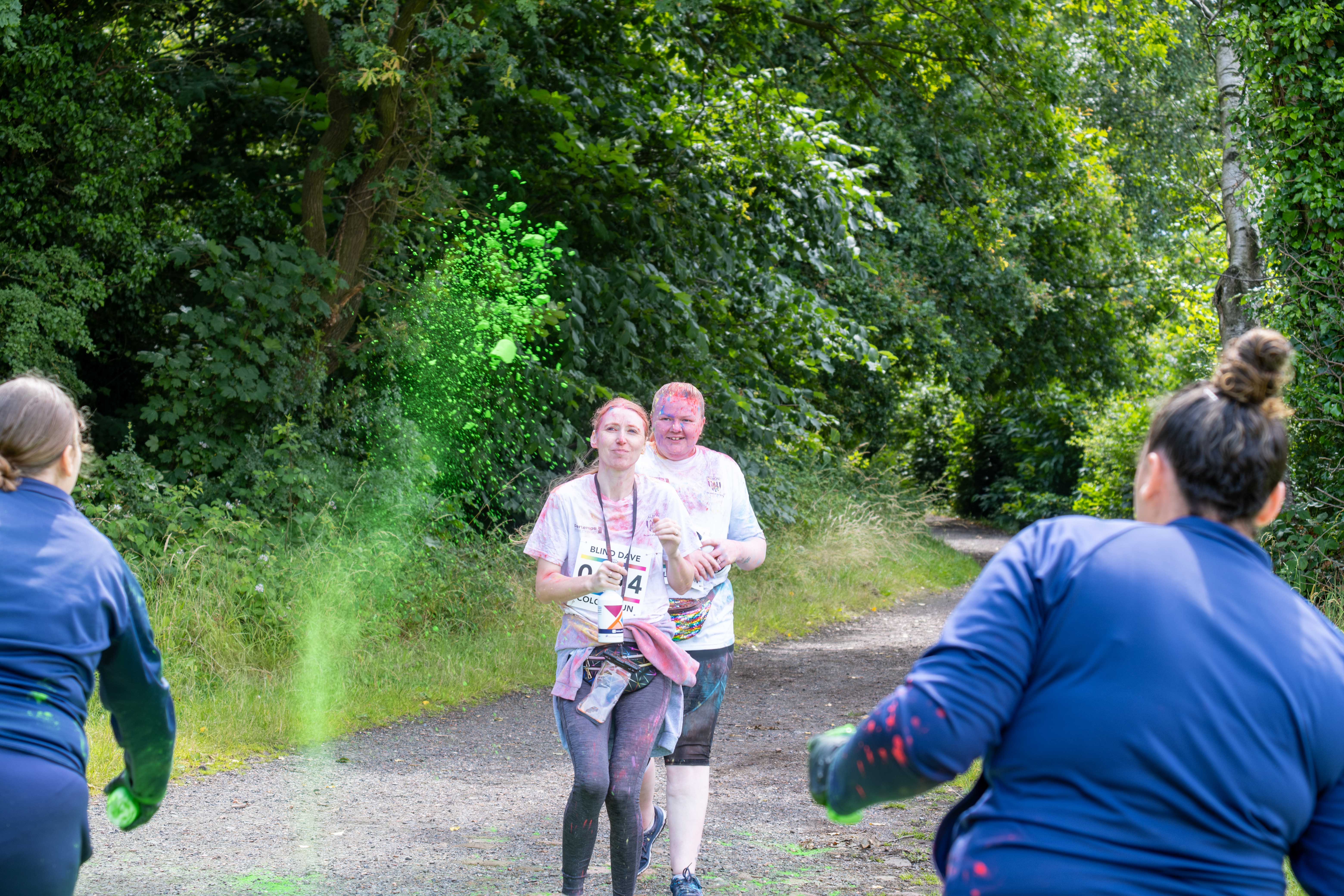 Two participants running towards Foundation staff at a colour station, throwing paint powder.