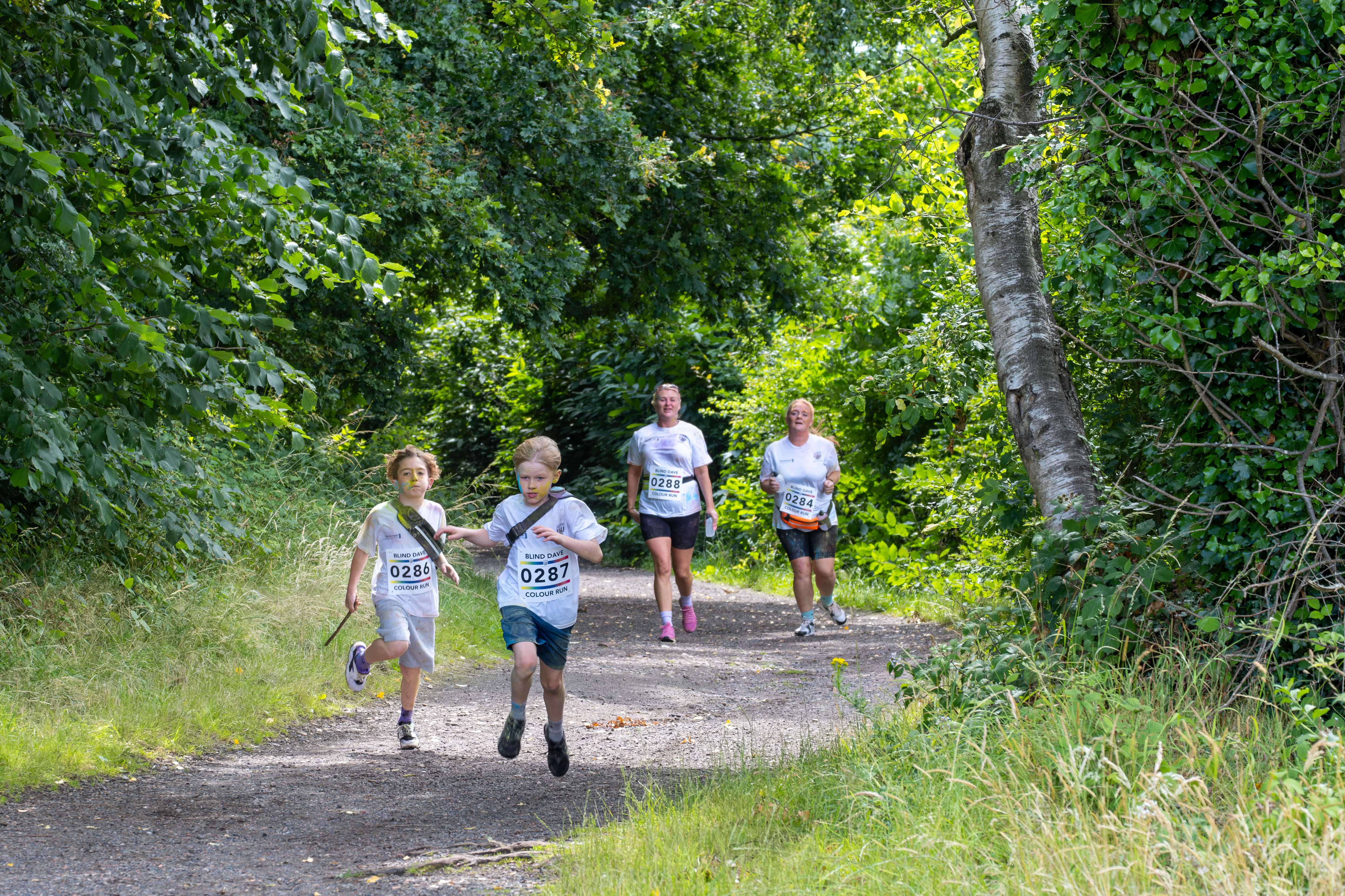 Four participants running the Sandwell Valley path, surrounded by trees.