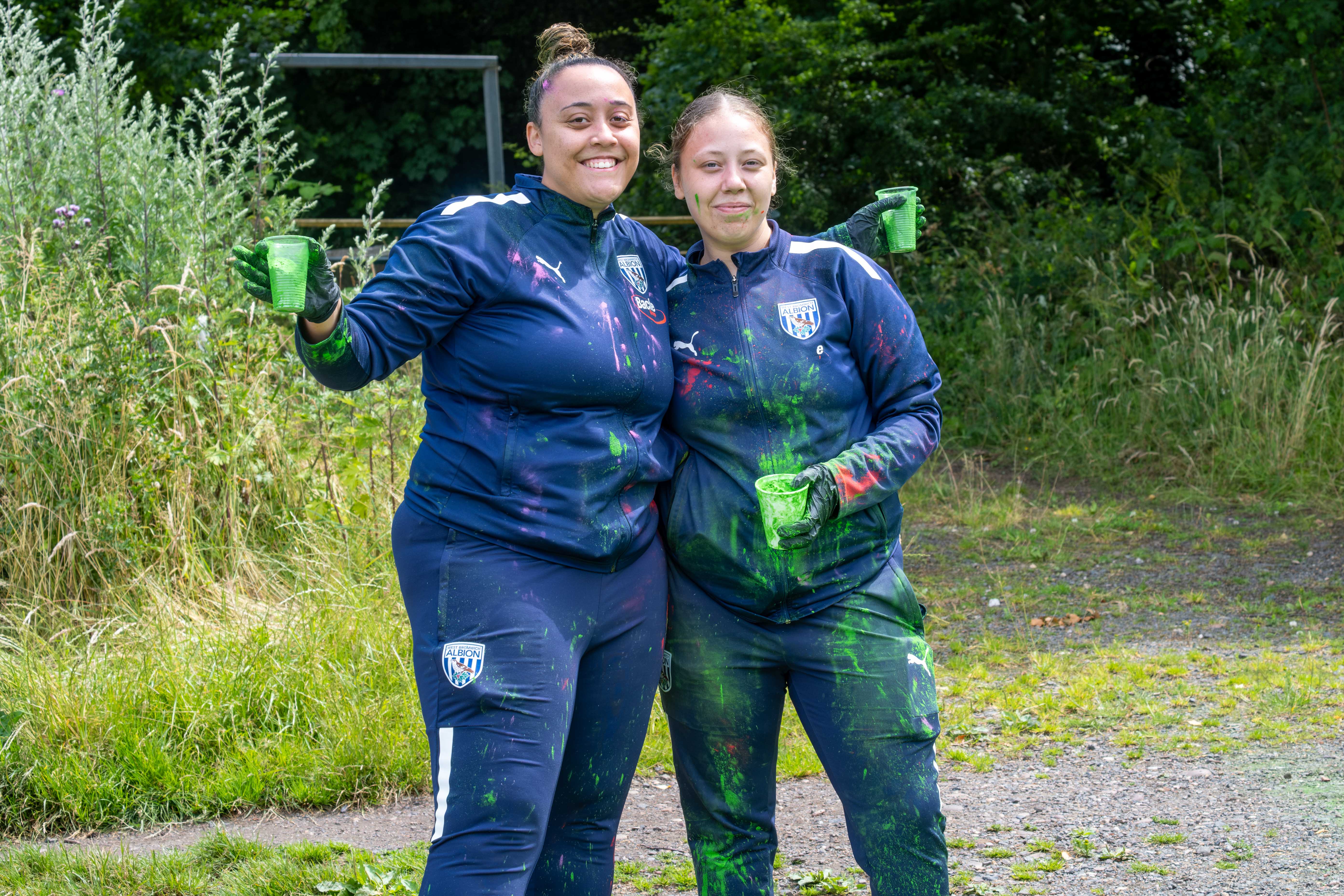 Two Foundation staff members posing for photo, holding cups of green paint powder.