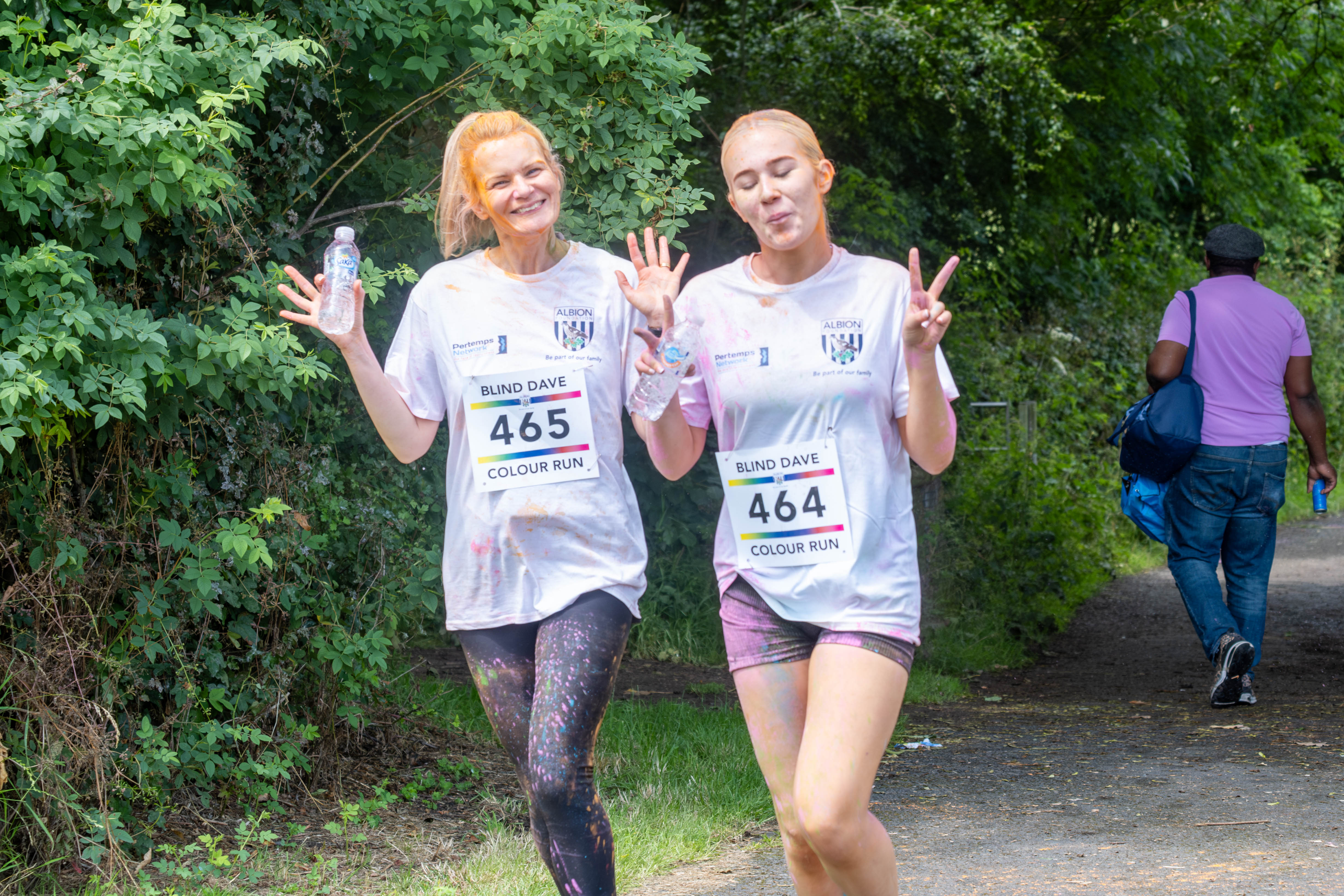 Two female participants holding water bottles and smiling showing peace sign .