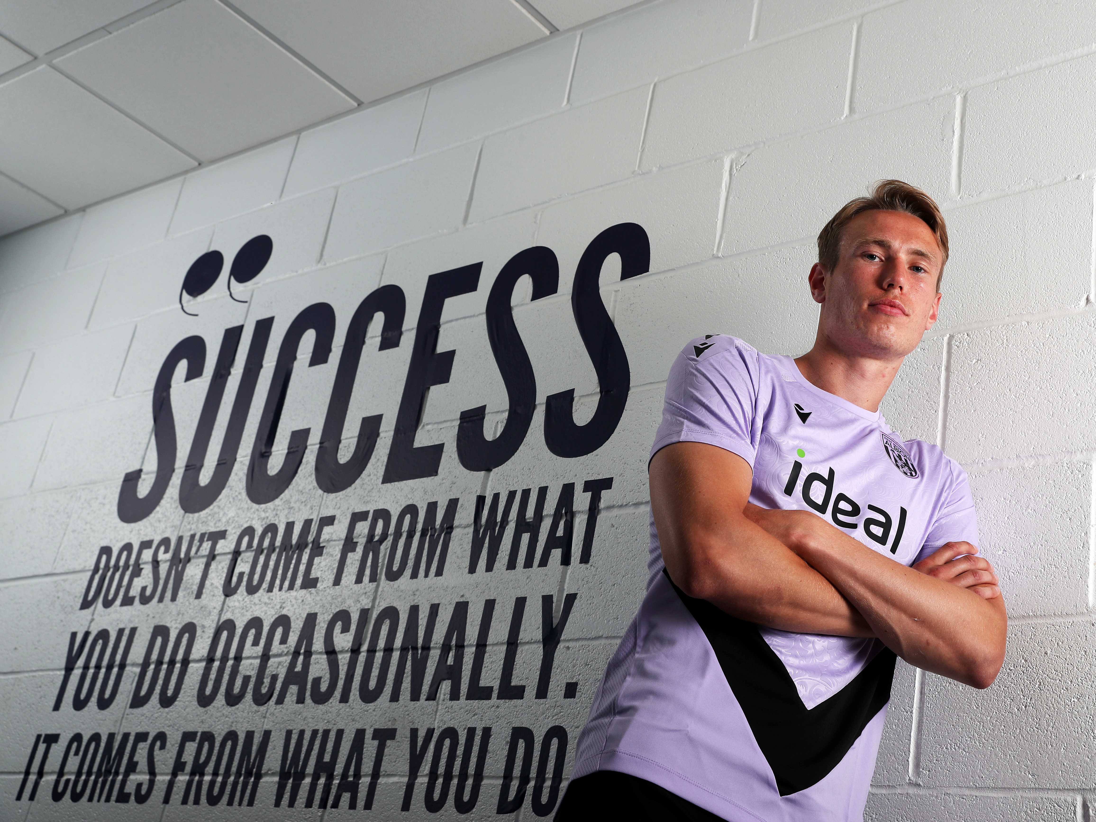 Torbjørn Heggem posing for a photo while stood against a wall with motivational writing on