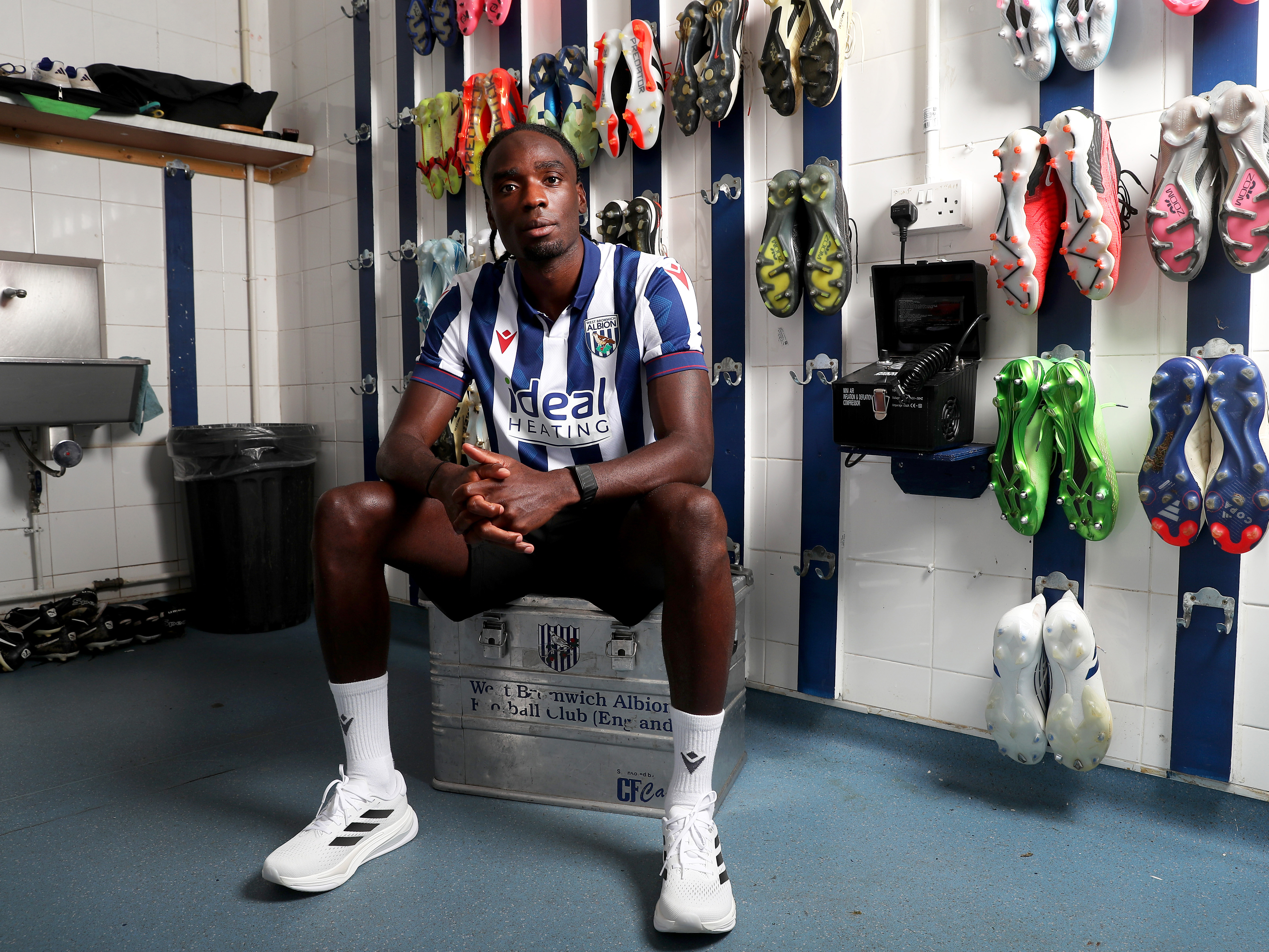 Devante Cole sat in the boot room at the training ground wearing a home shirt looking at the camera 