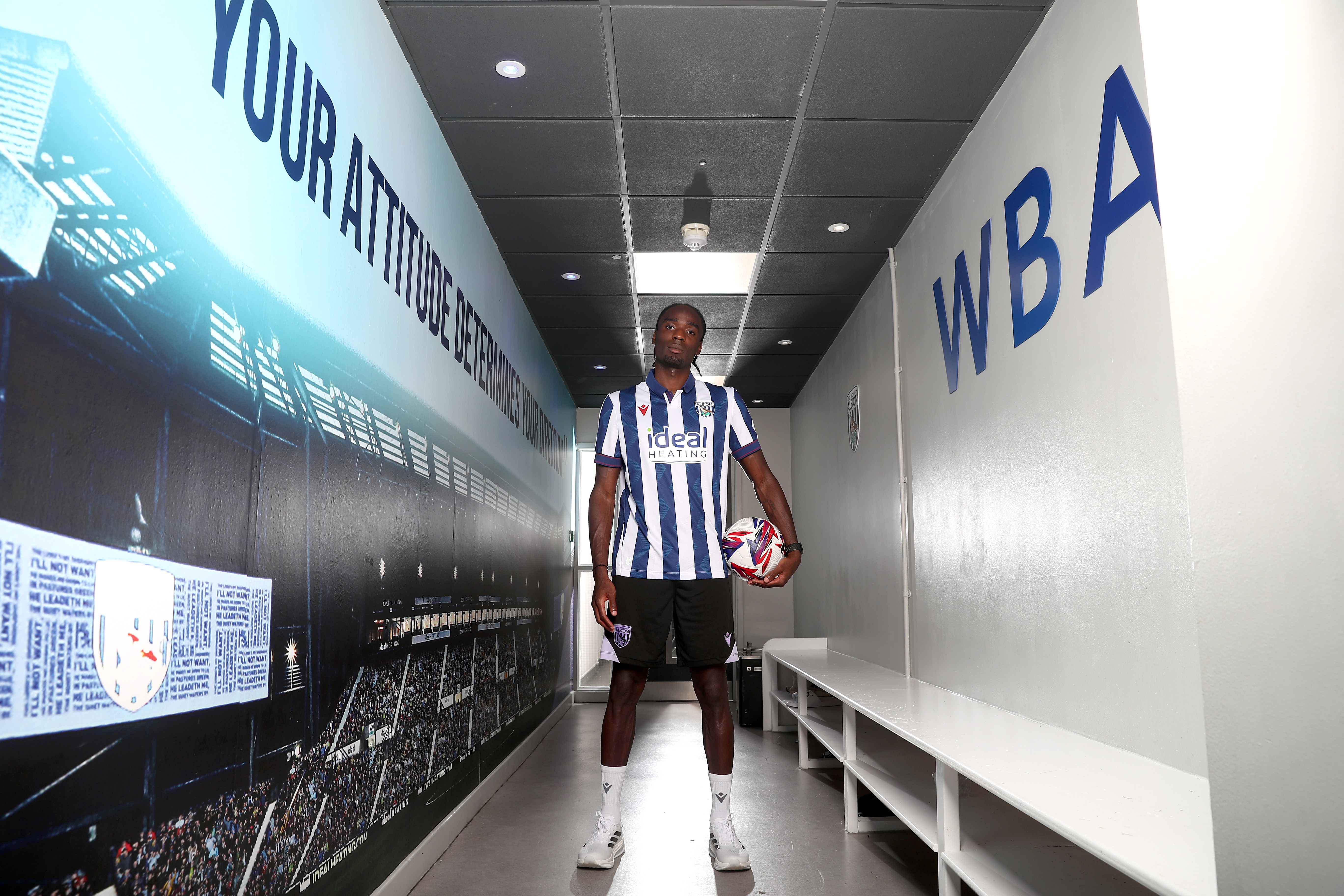 Devante Cole smiling at the camera stood in a corridor in the home shirt with a ball in his grasp