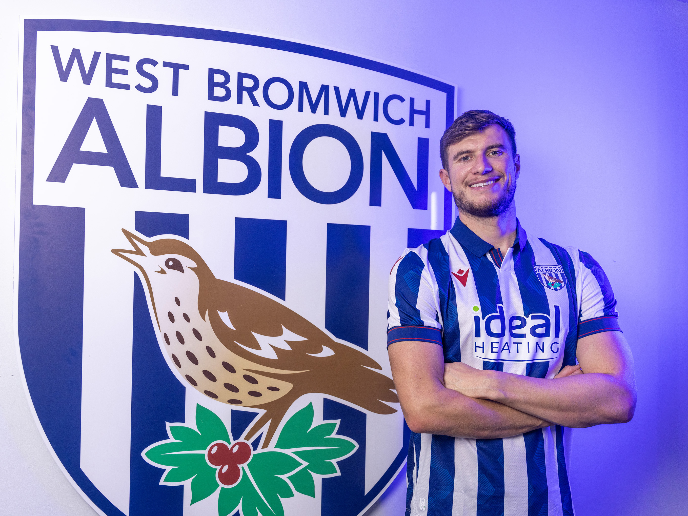 Paddy McNair smiling at the camera while stood in a home shirt in front of an Albion badge 