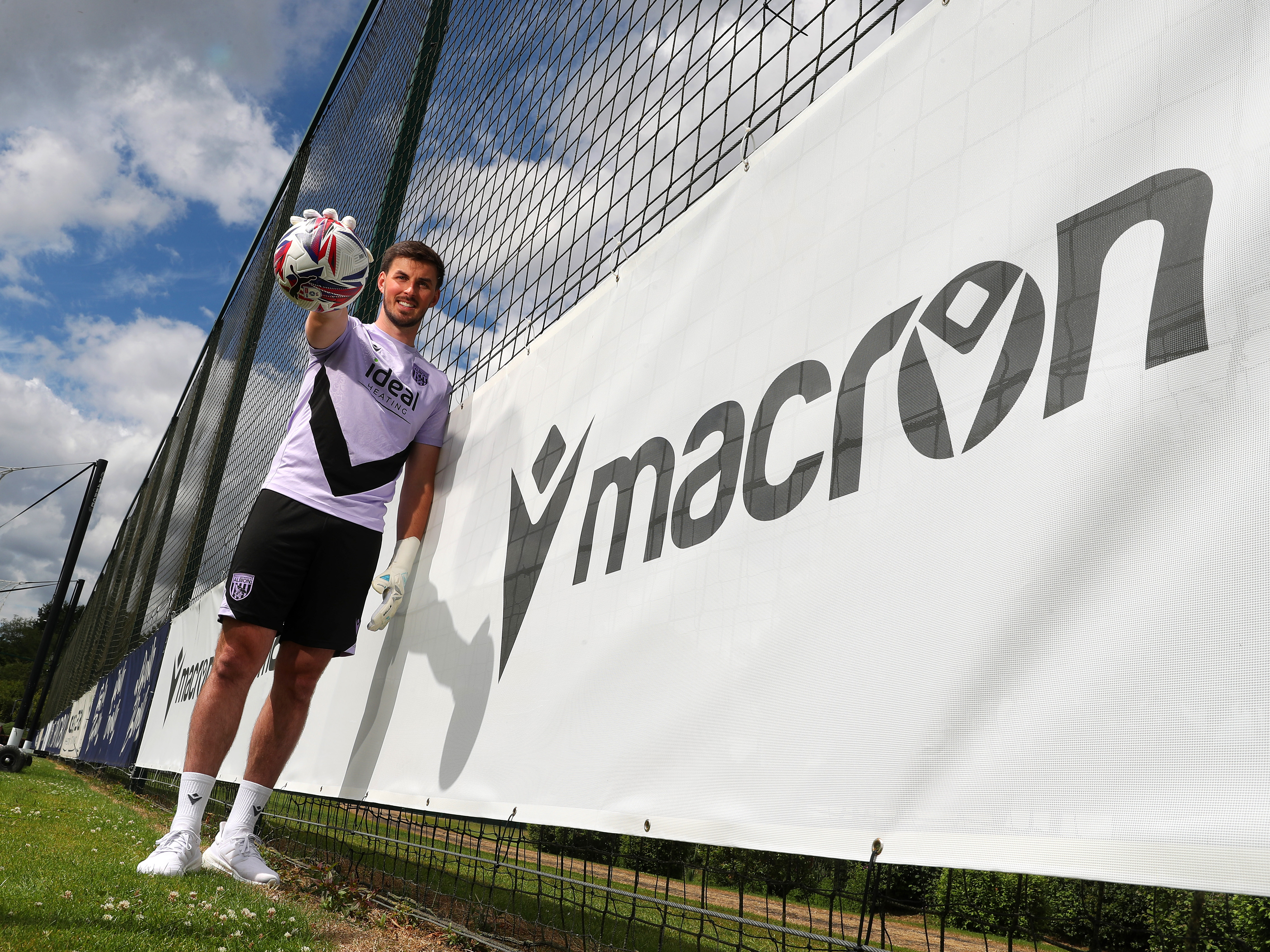 An image of Joe Wildsmith holding a football next to a Macron banner at the training ground