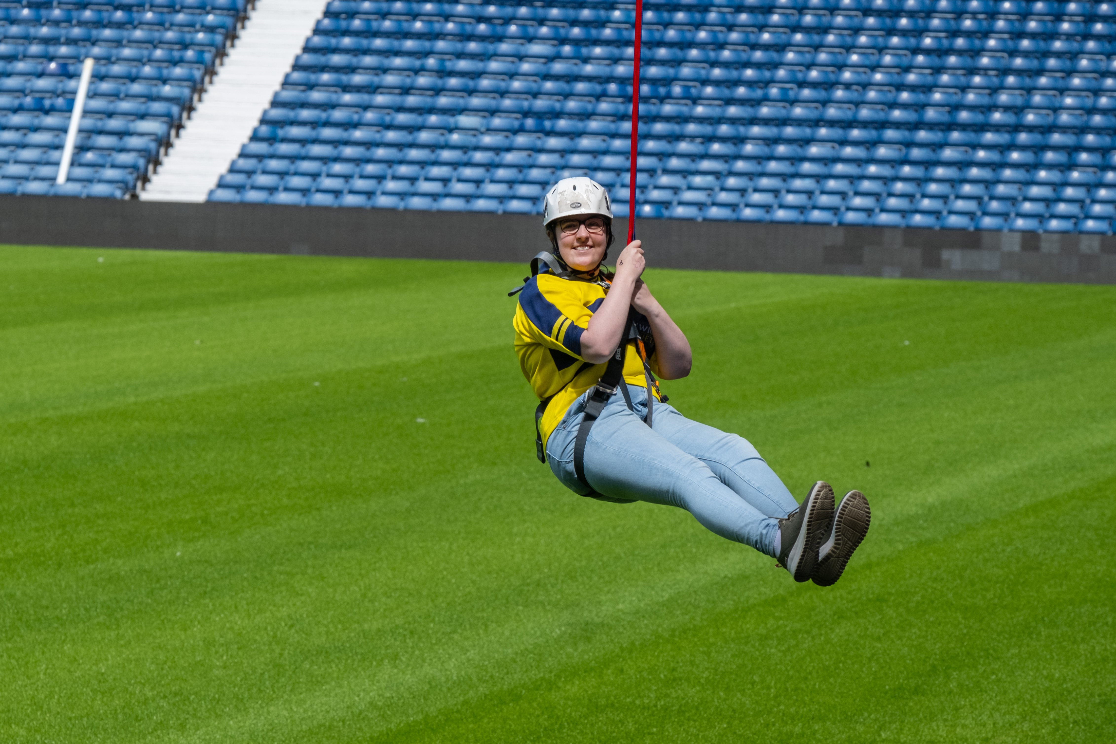 A participant wearing a classing Albion shirt heads across the pitch on the Zipwire whilst wearing a classic yellow Baggies shirt.