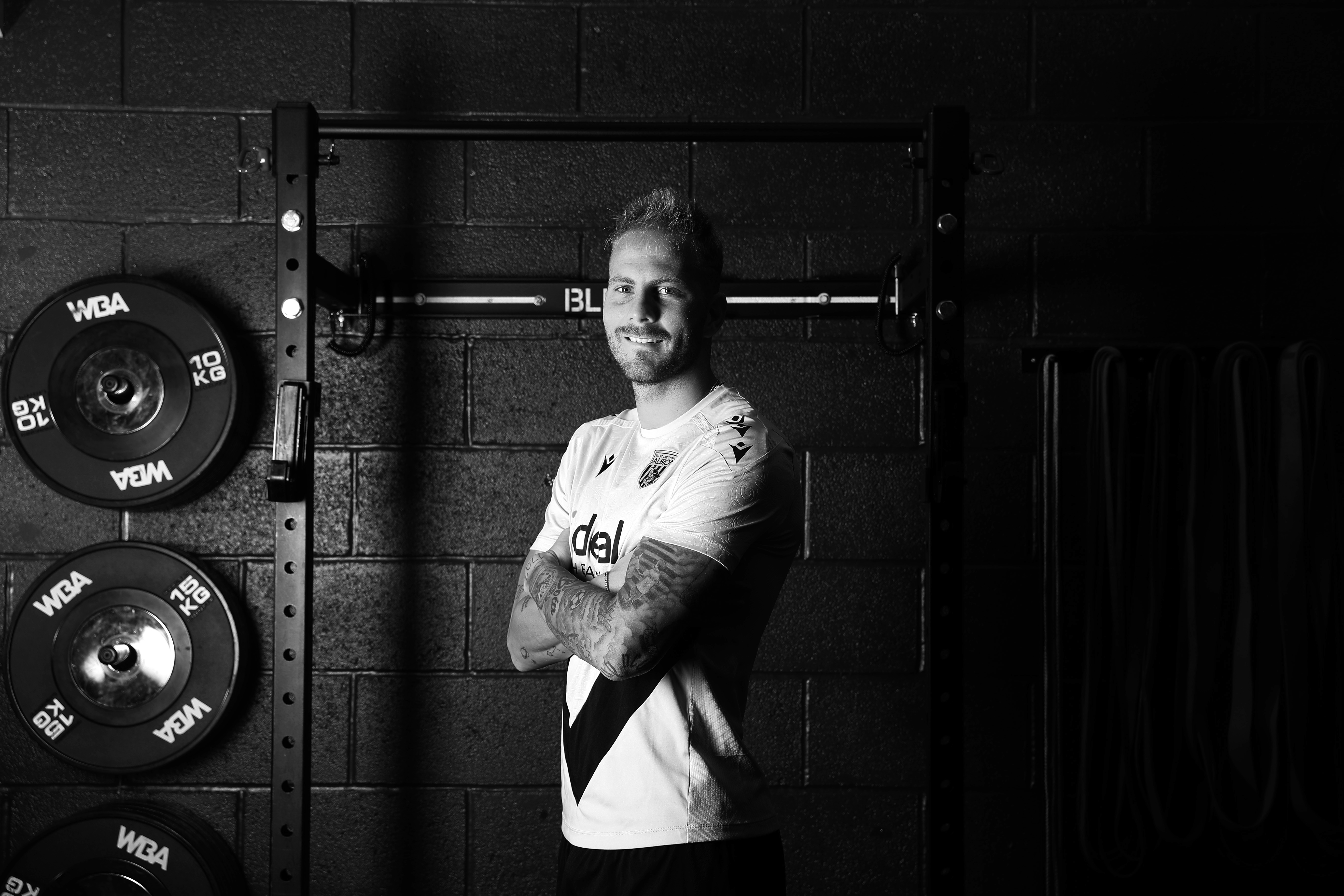 A black and white image of Uroš Račić smiling at the camera while stood in the gym