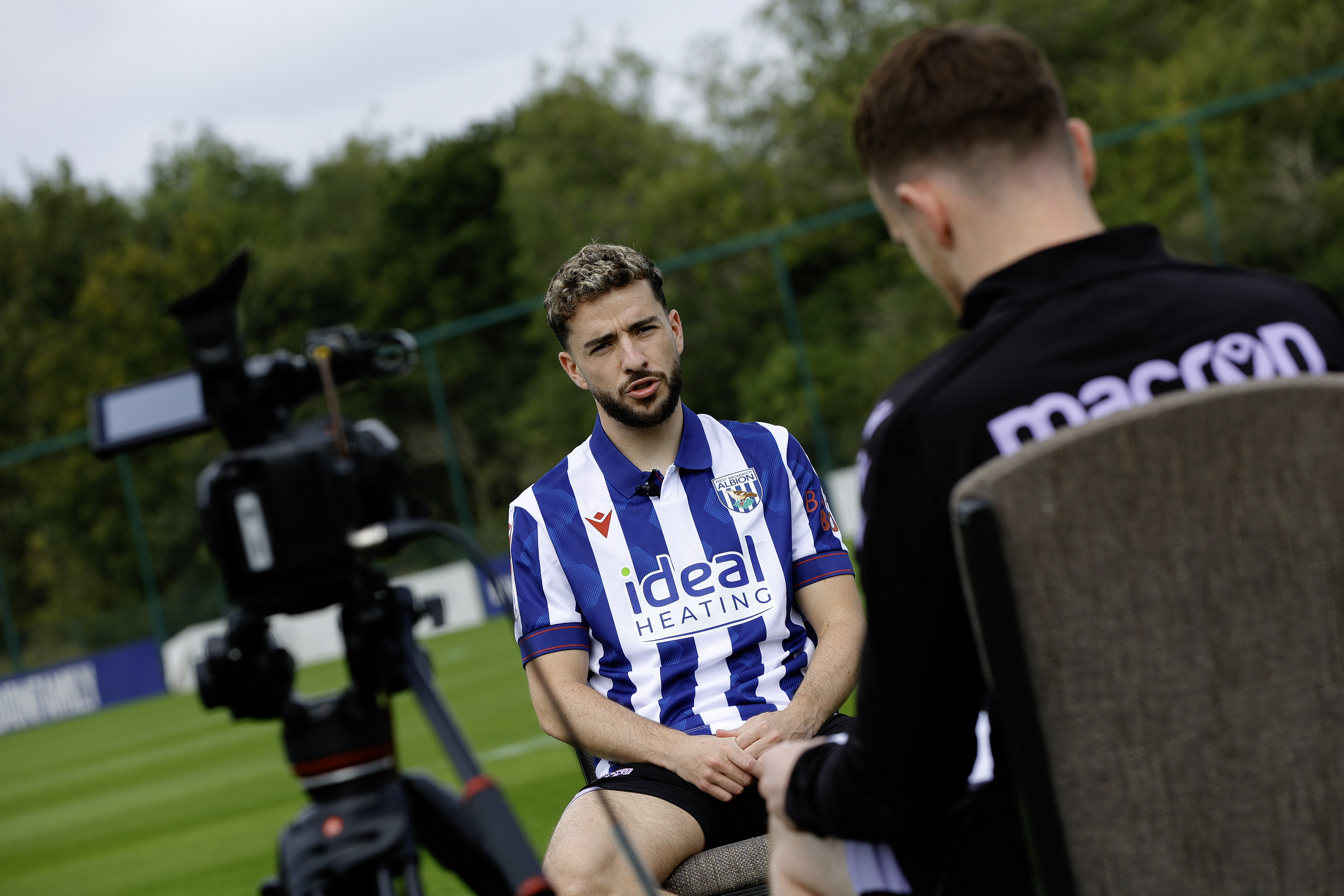 Mikey Johnston is interviewed while sat in a chair in the home shirt on a training pitch 