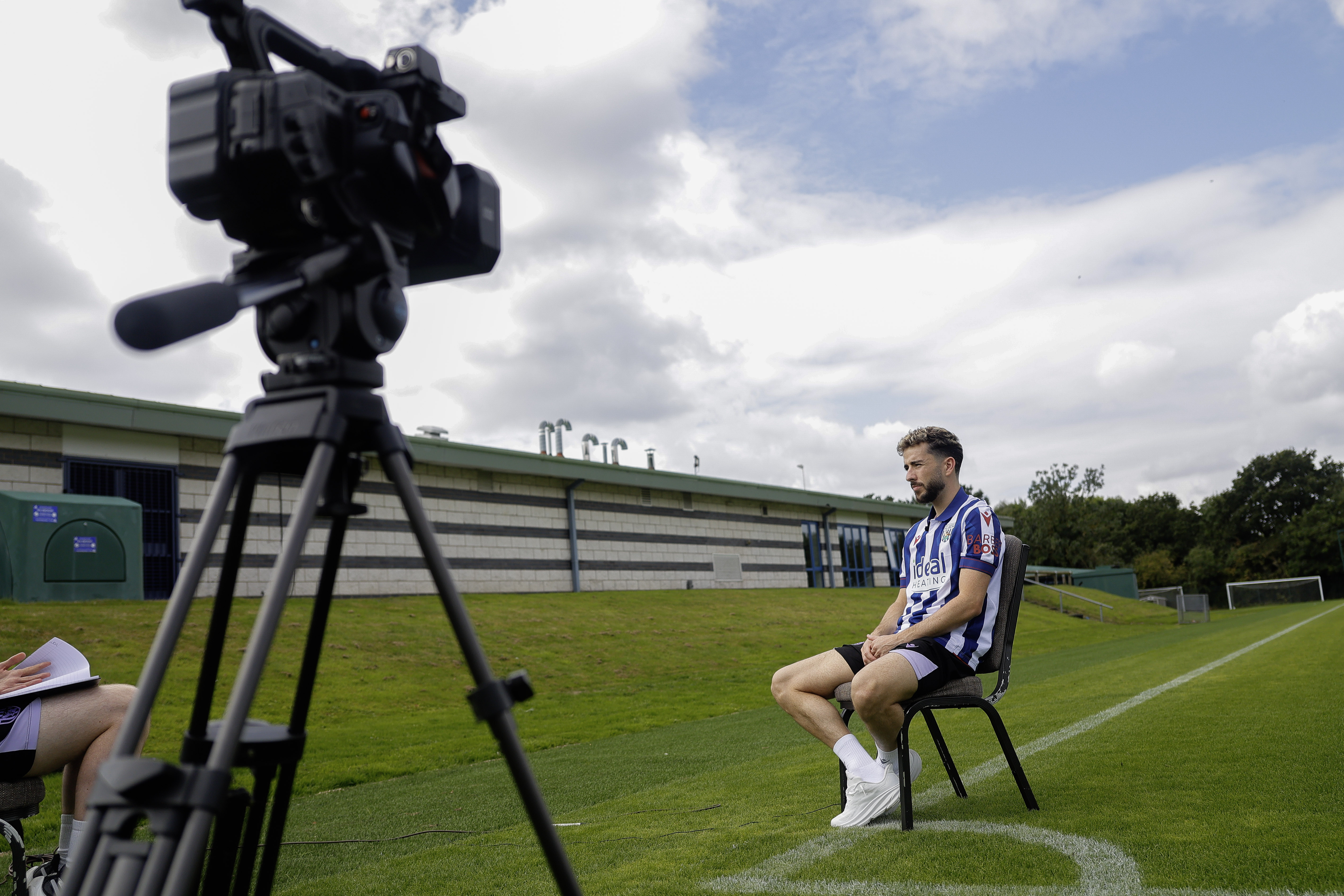 Mikey Johnston is interviewed while sat in a chair in the home shirt on a training pitch 