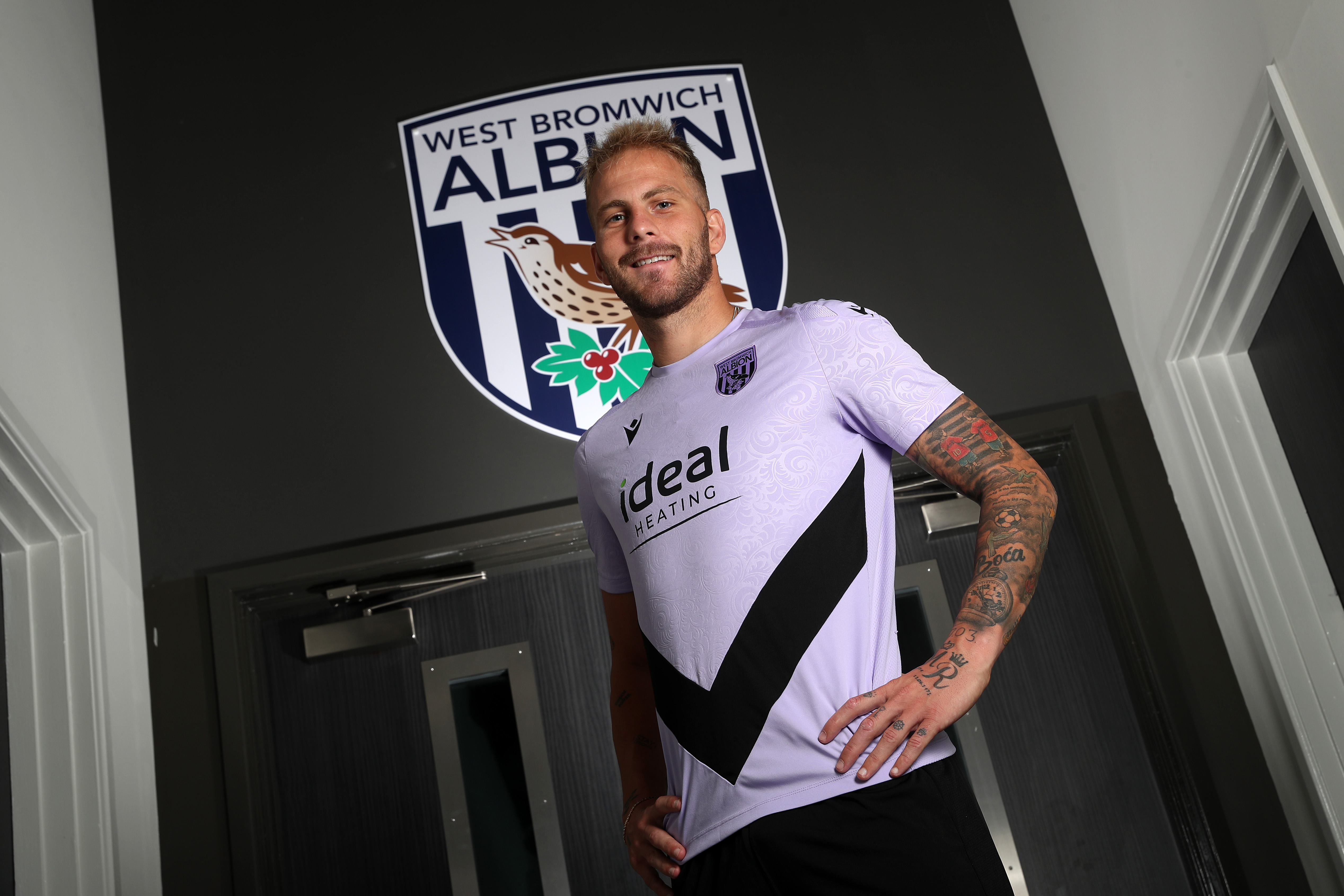 Uroš Račić smiling at the camera while stood in front of an Albion badge 