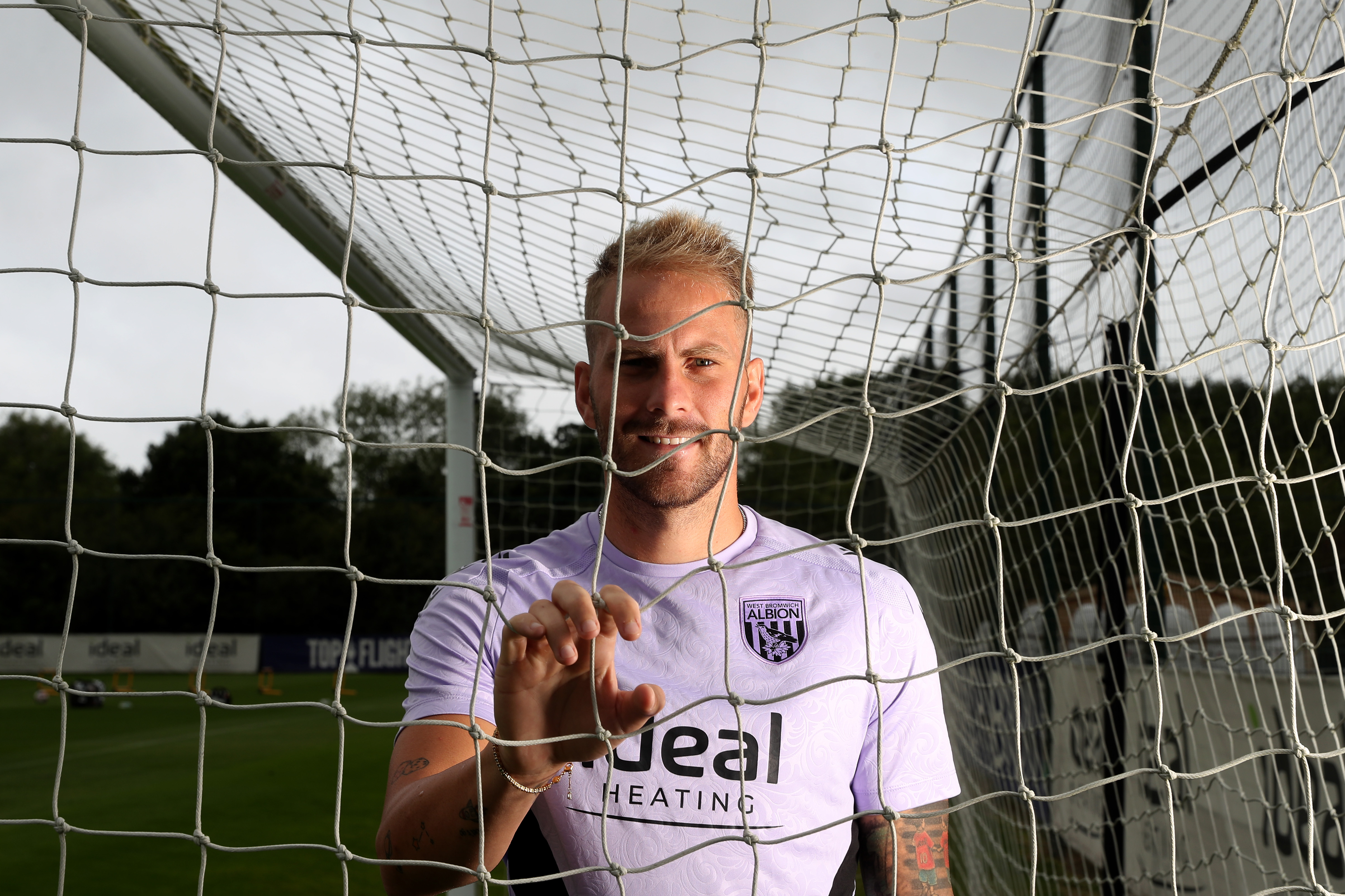 Uroš Račić smiling at the camera while looking through and holding on to a goal net 