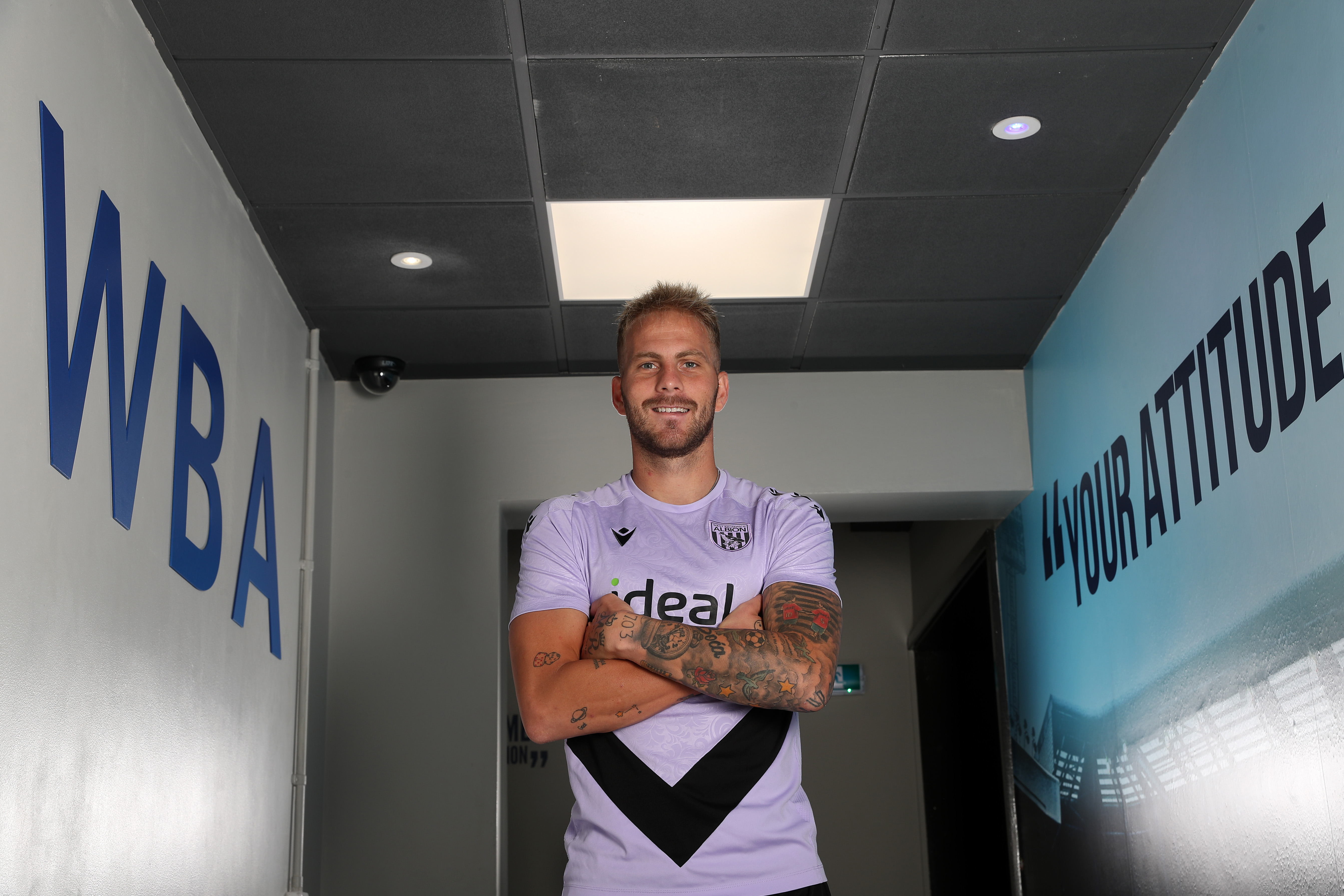 Uroš Račić smiling at the camera while stood in a corridor with his arms folded 