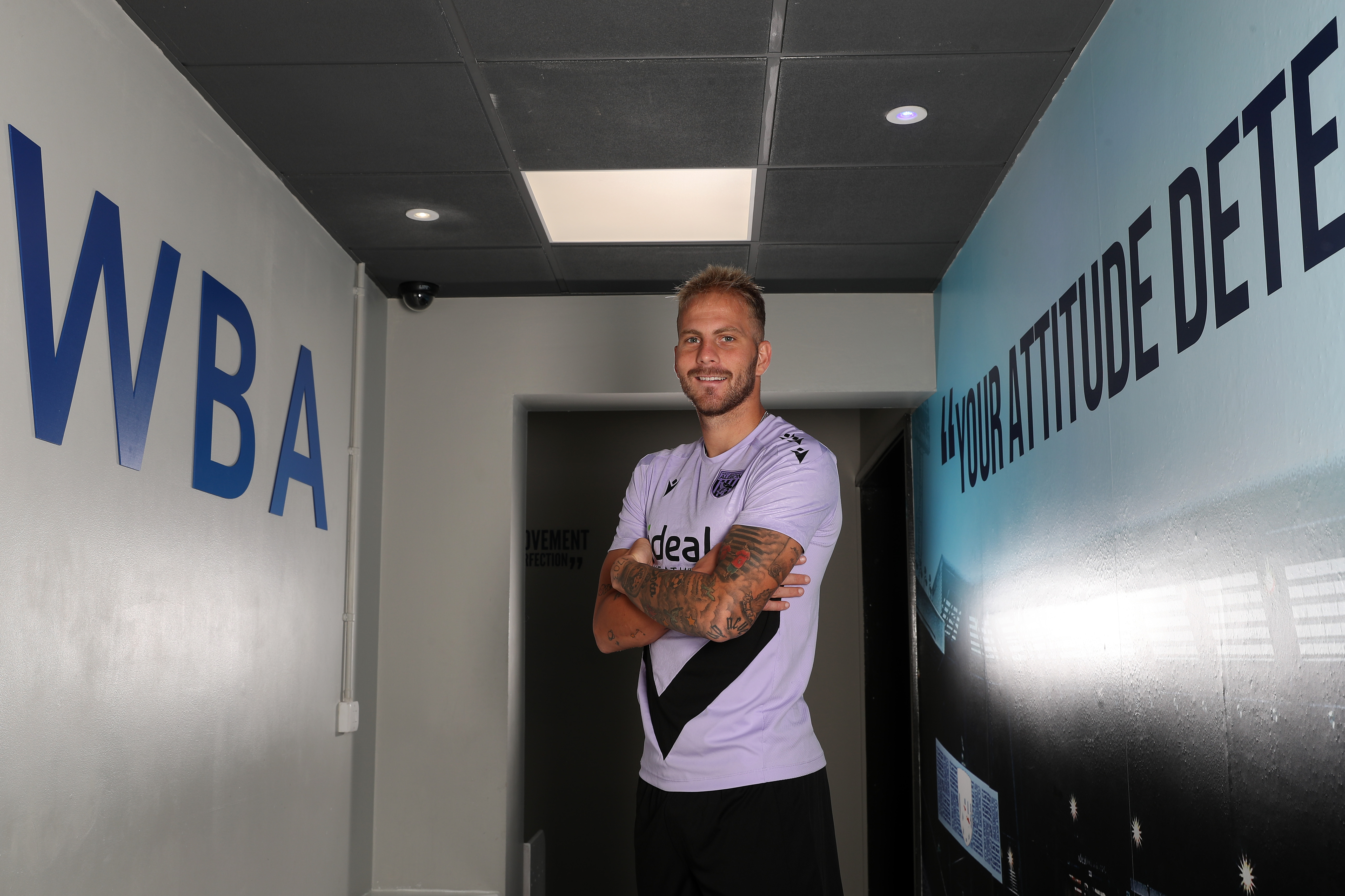 Uroš Račić smiling at the camera while stood in a corridor with his arms folded 