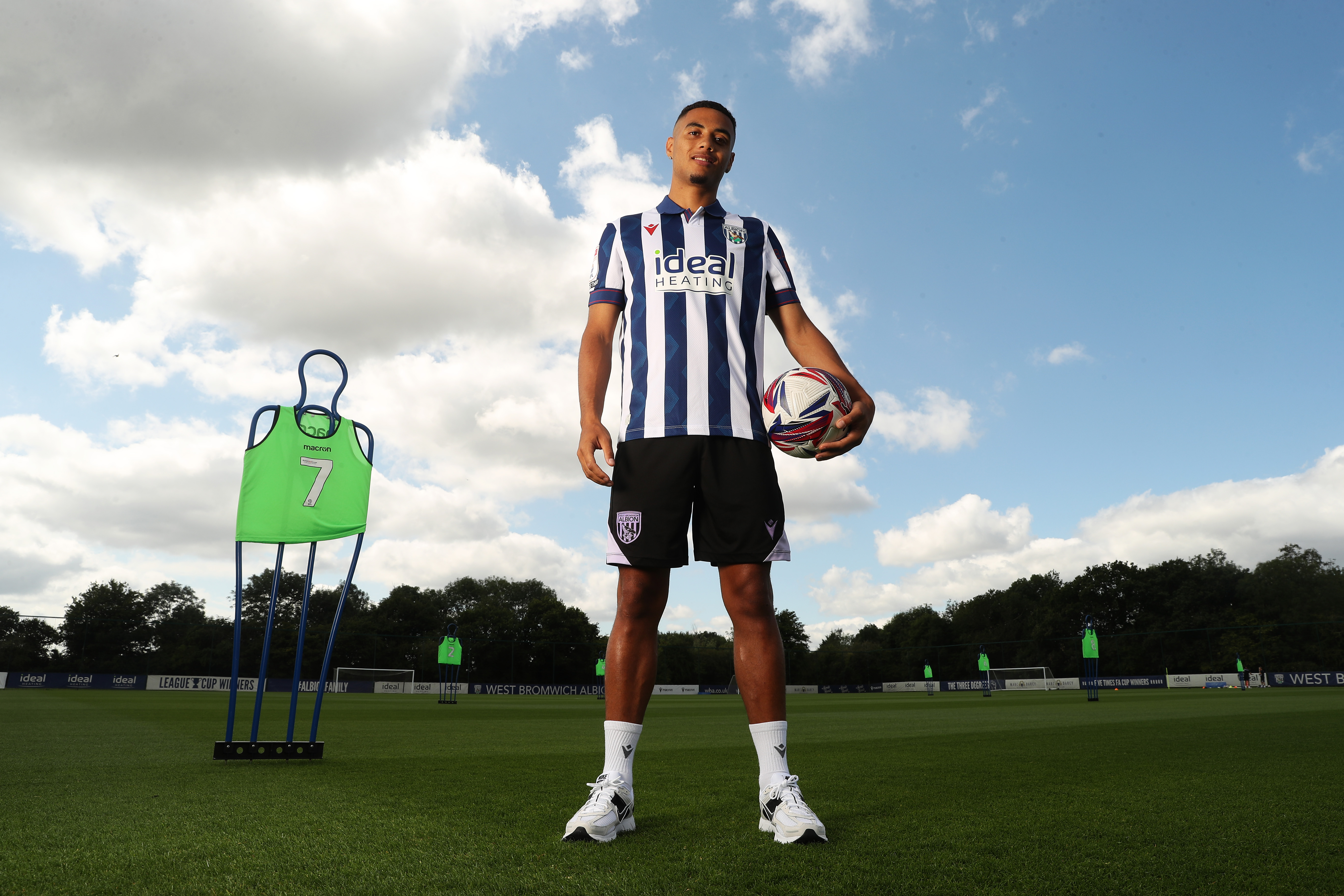 Lewis Dobbin smiling at the camera while stood on the training pitch in a home shirt holding a ball