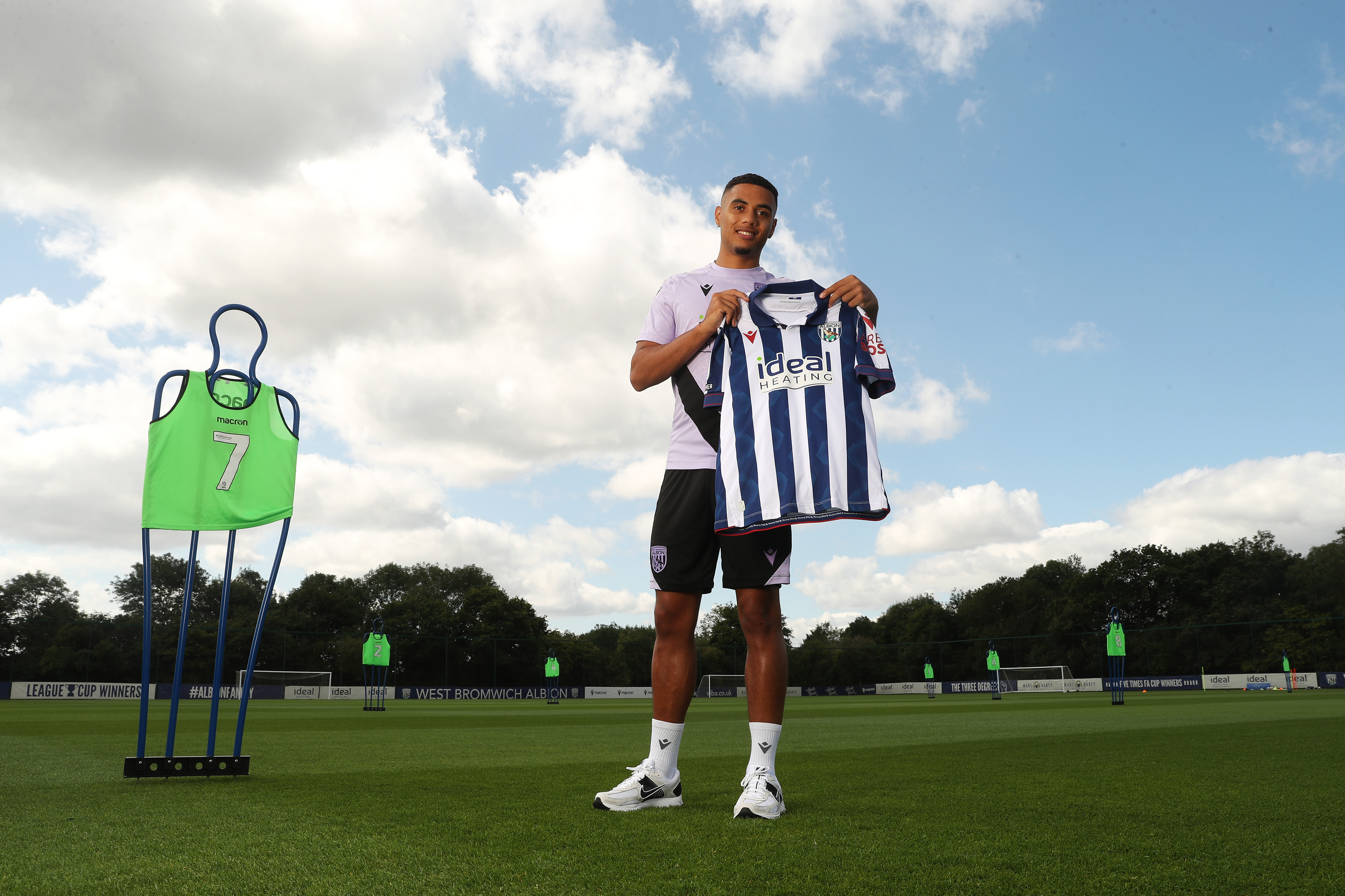 Lewis Dobbin smiling at the camera while holding a home shirt up while stood on a training pitch 