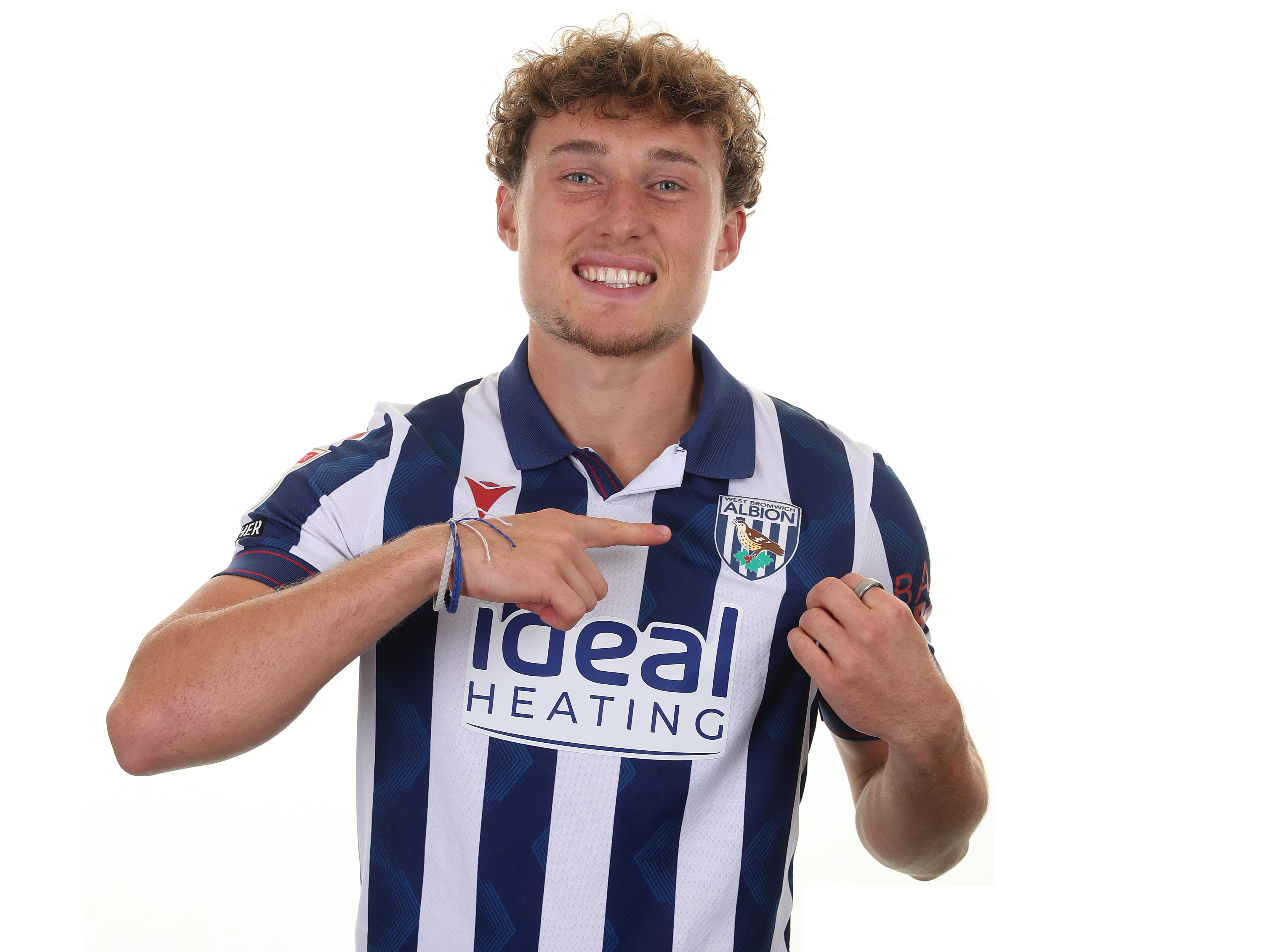 Callum Styles smiling at the camera while wearing a home shirt and pointing to the badge 