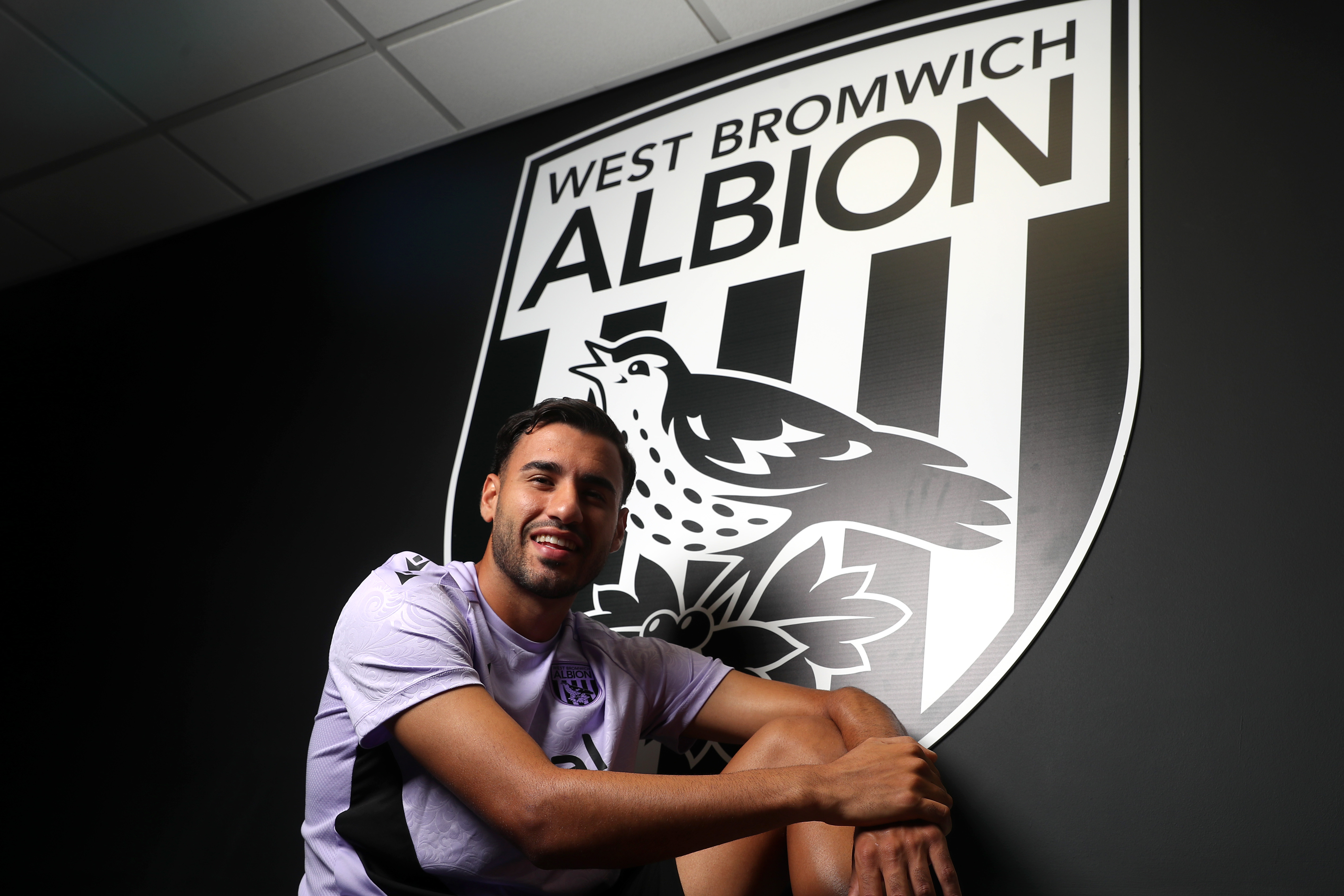 Gianluca Frabotta smiling at the camera while sat under a WBA badge 