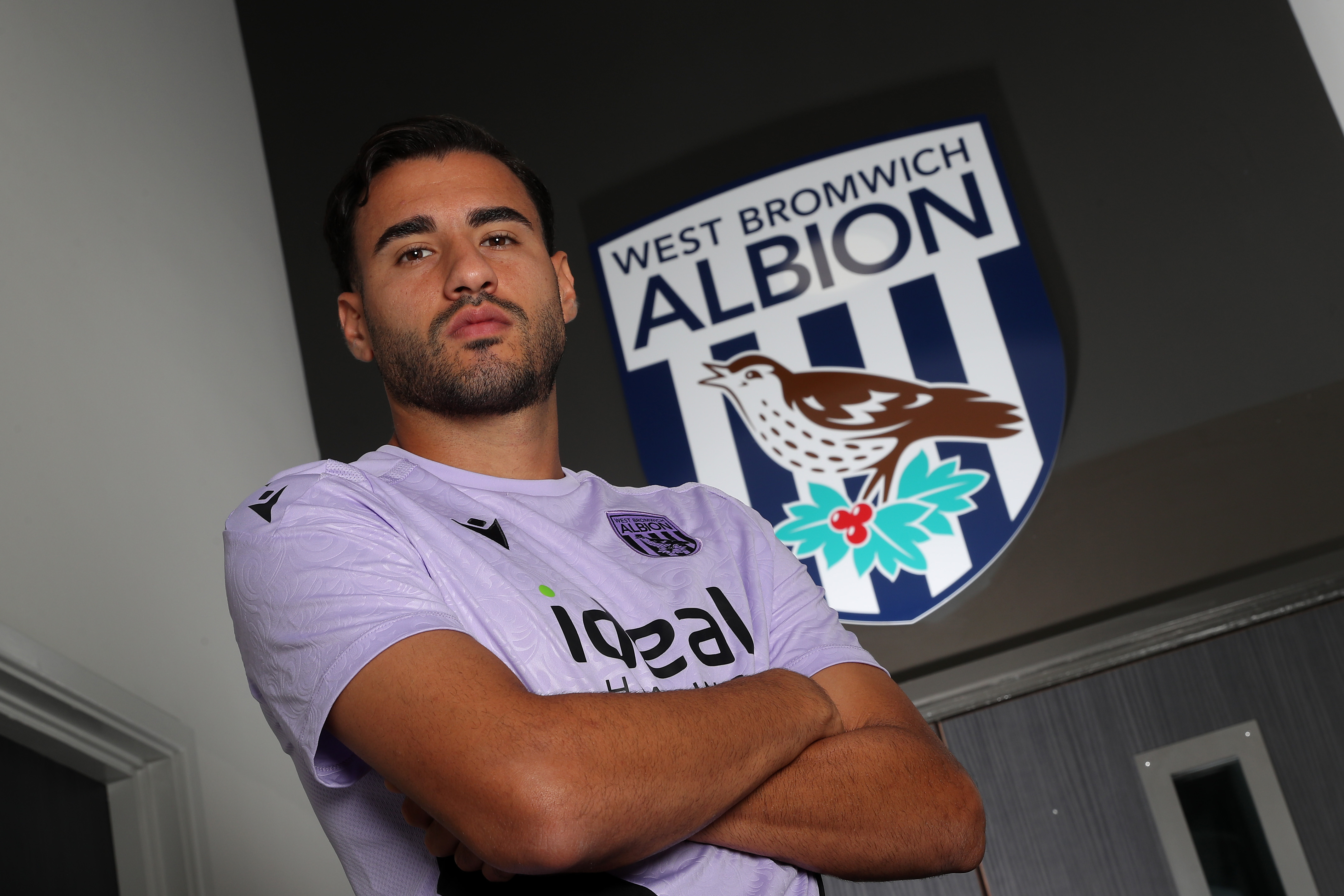 Gianluca Frabotta looking at the camera with his arms crossed while stood under a WBA badge 