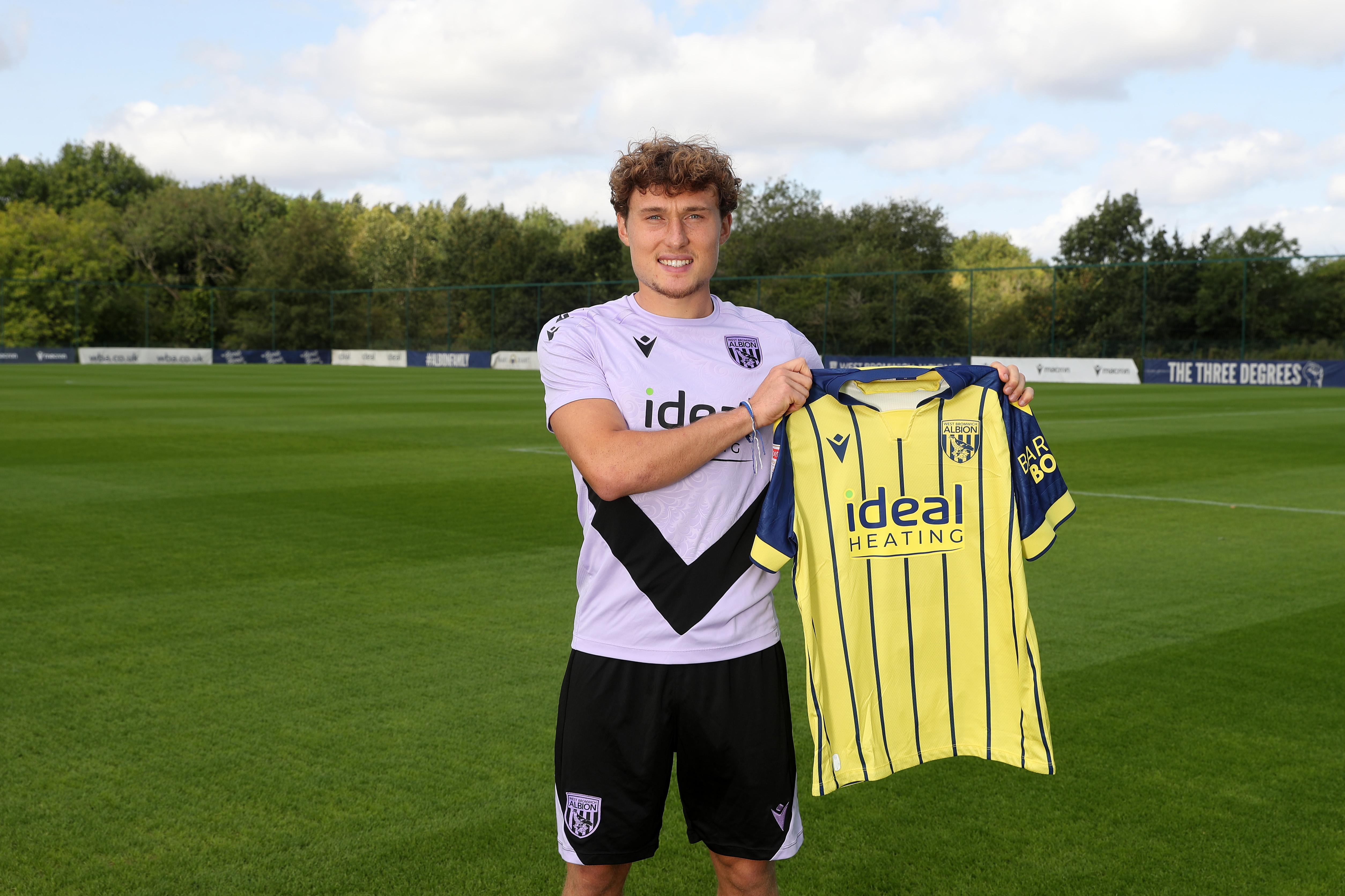 Callum Styles smiling at the camera while holding a yellow away shirt 