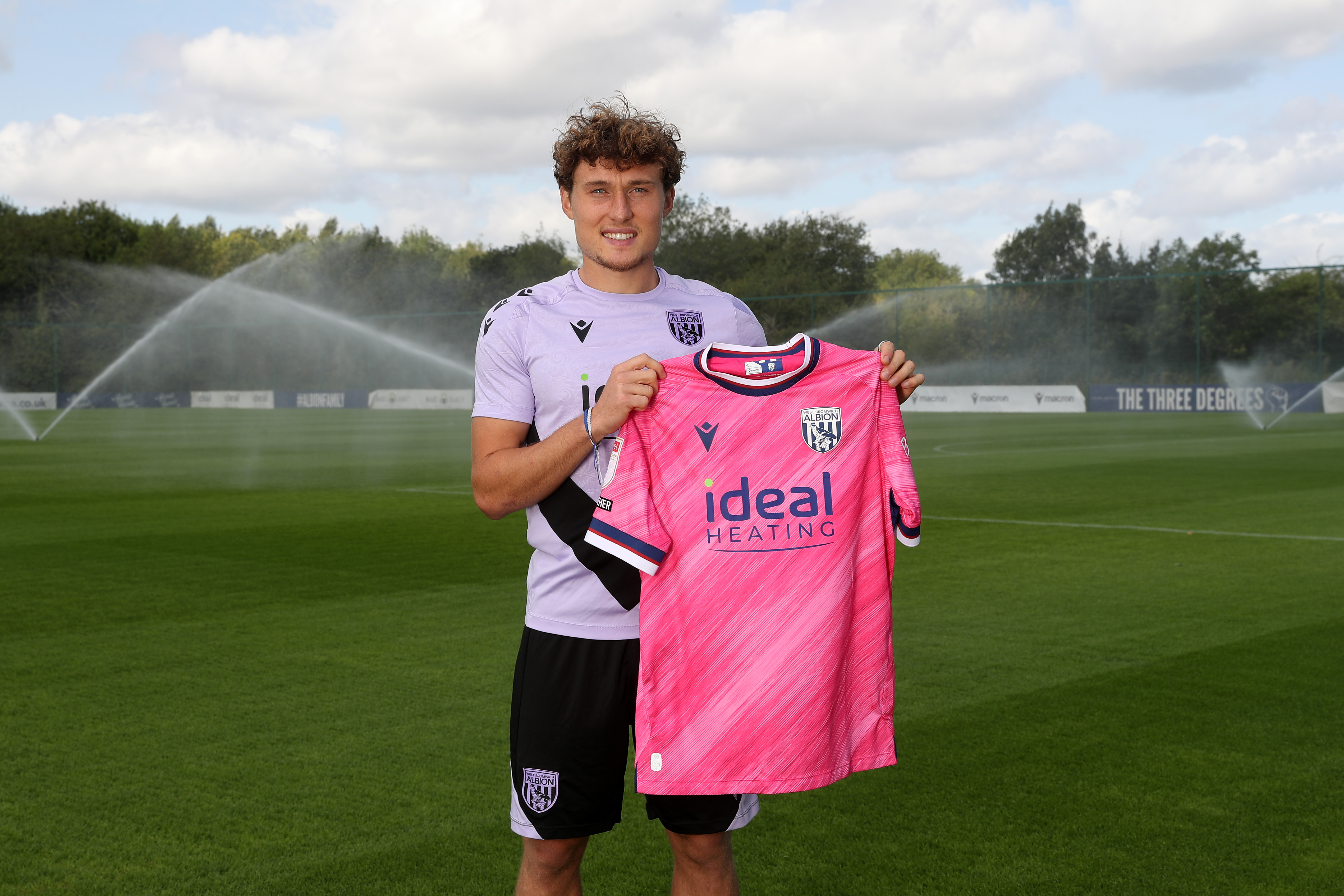 Callum Styles smiling at the camera while holding a pink away shirt 