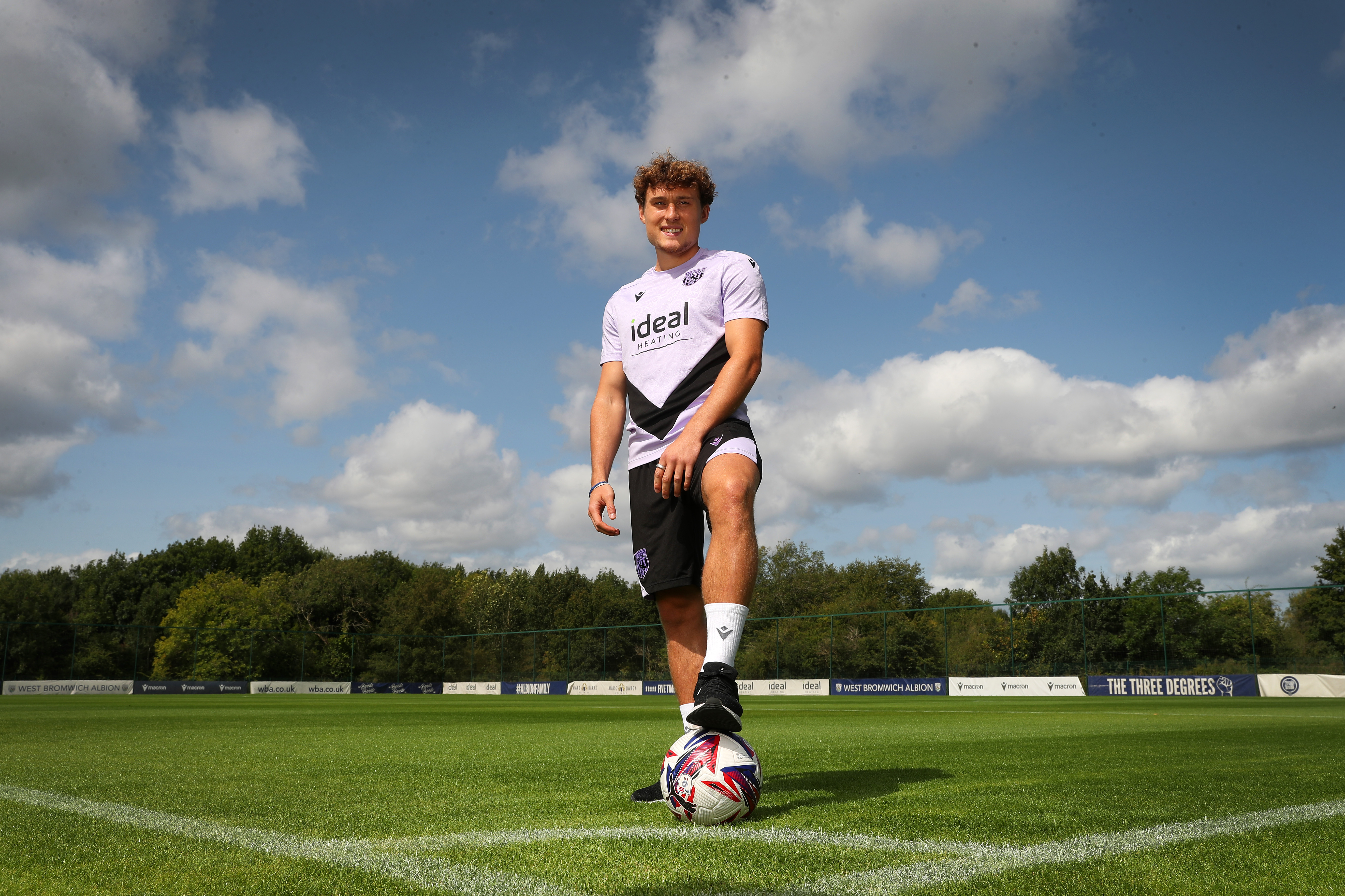 Callum Styles smiling at the camera with one foot on the ball out on the training pitch 