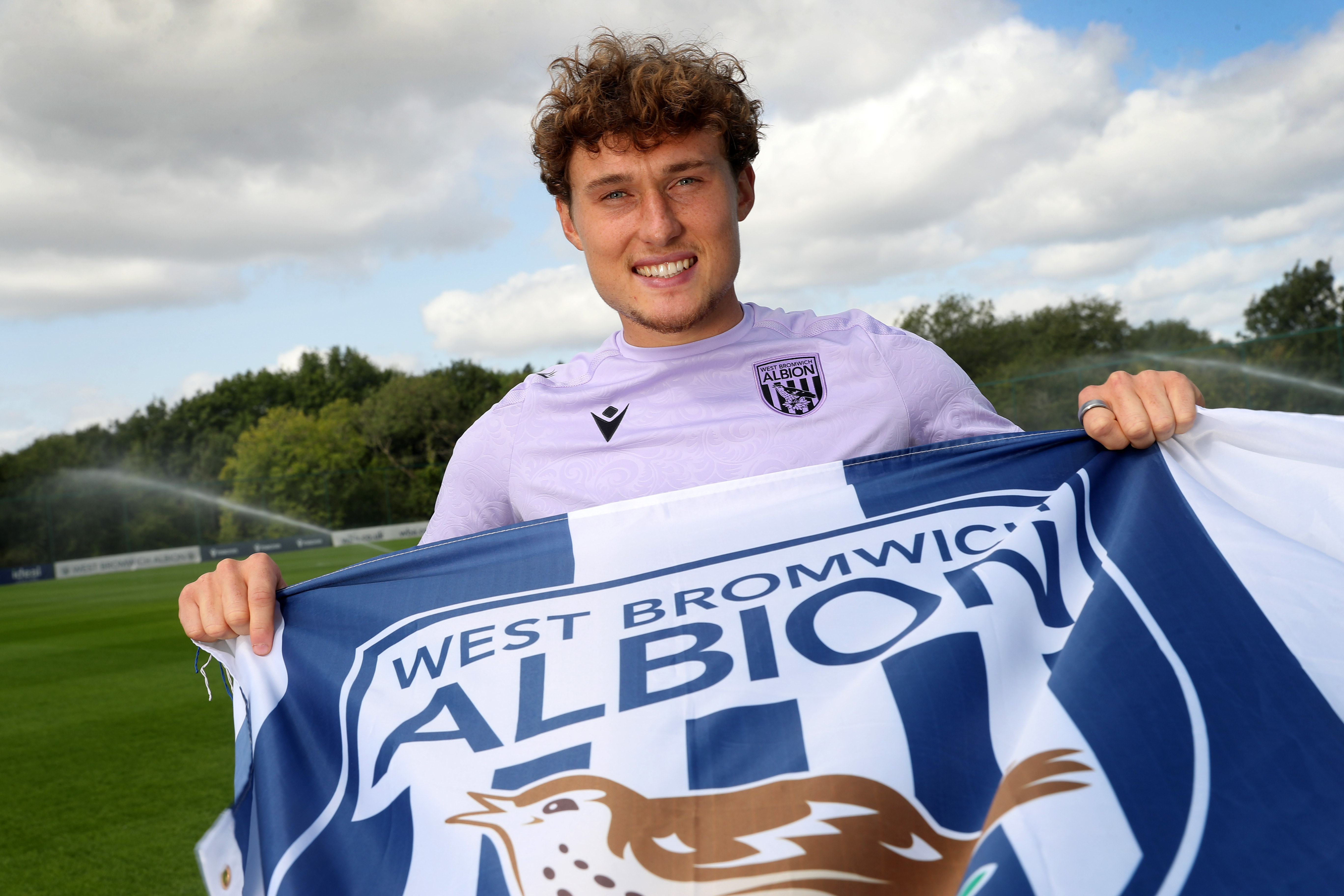 Callum Styles smiling at the camera while holding a WBA flag