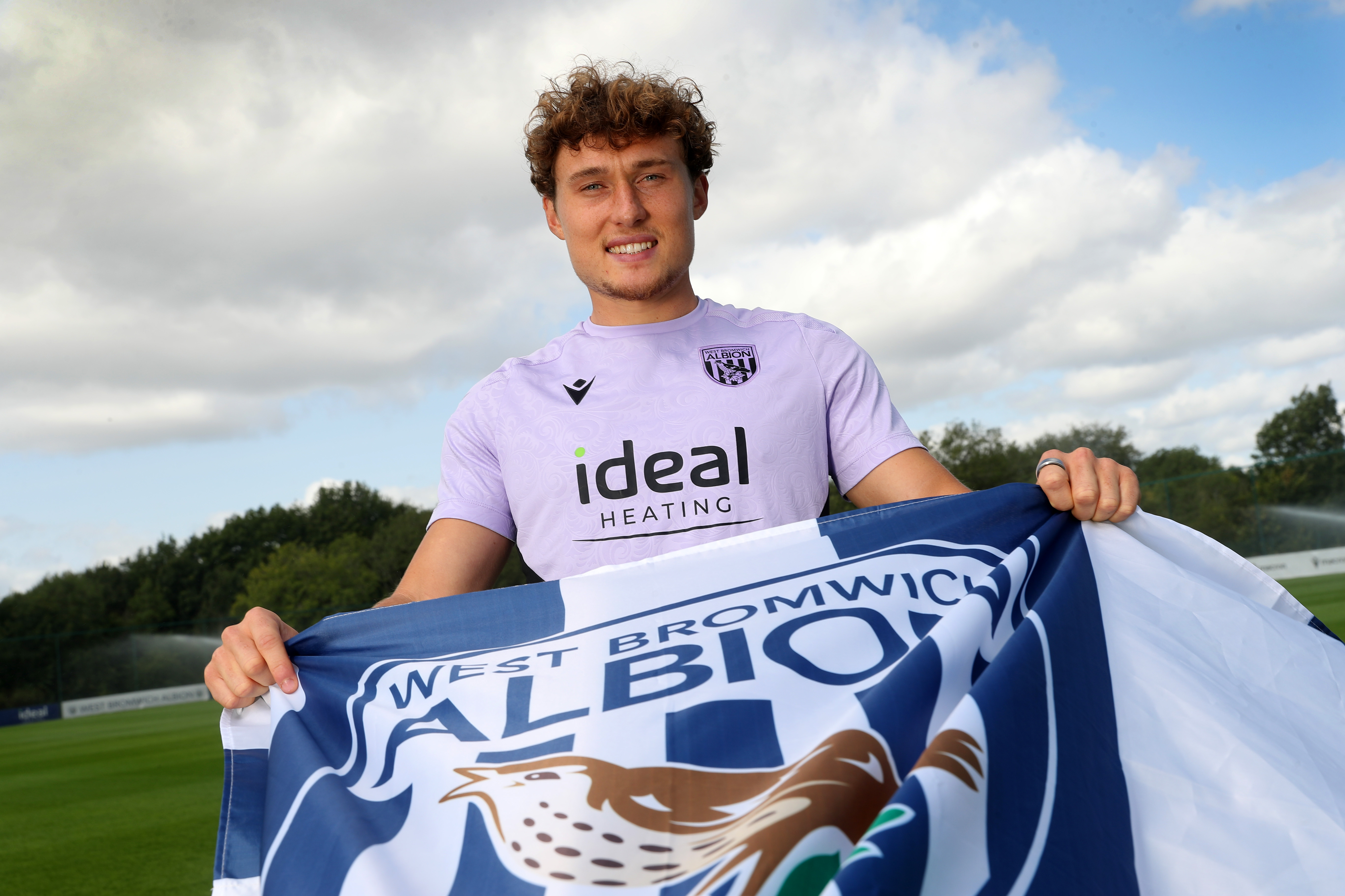 Callum Styles smiling at the camera while holding a WBA flag