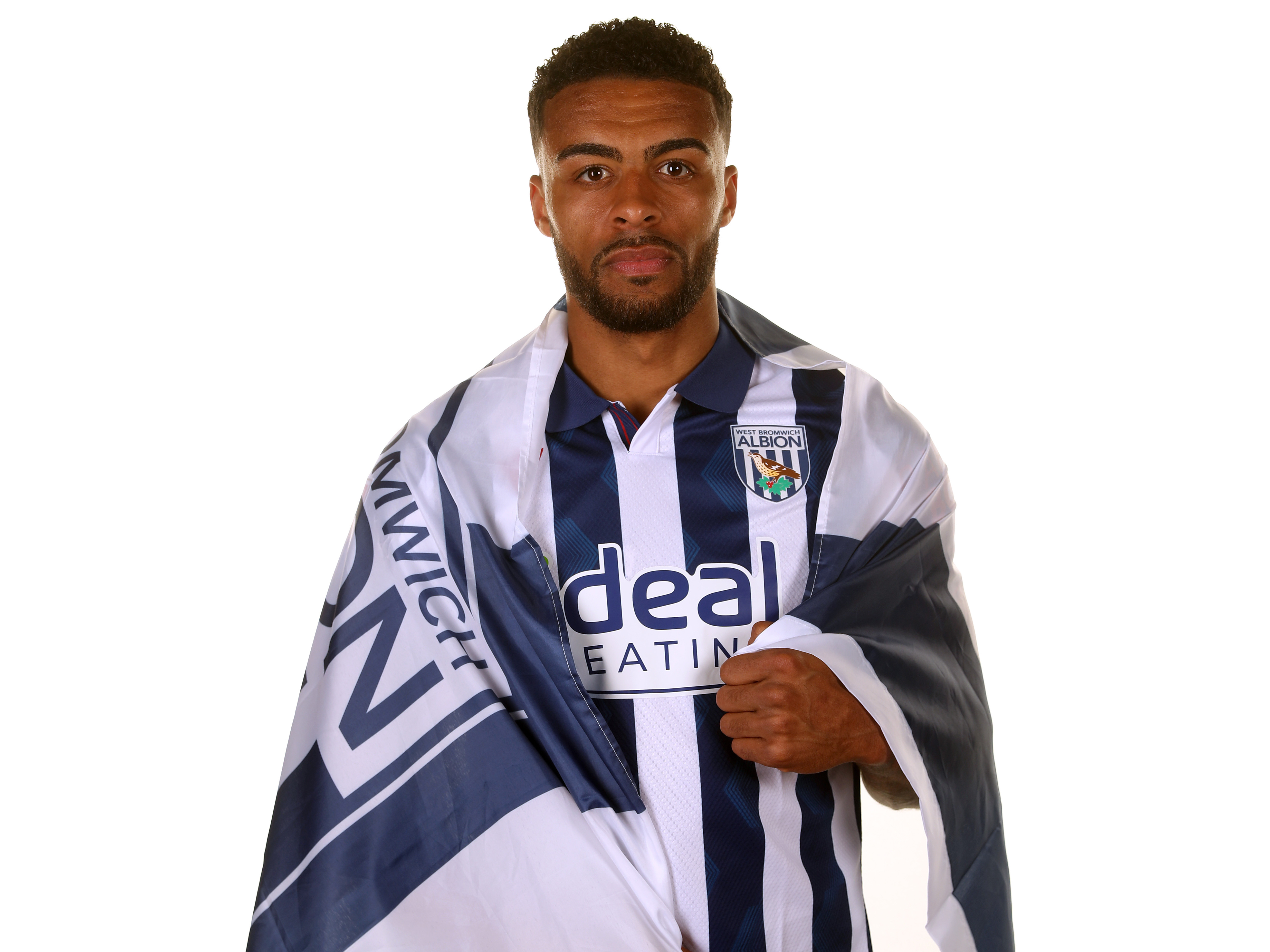 Darnell Furlong wrapped in a WBA flag while in a home shirt and looking at the camera 