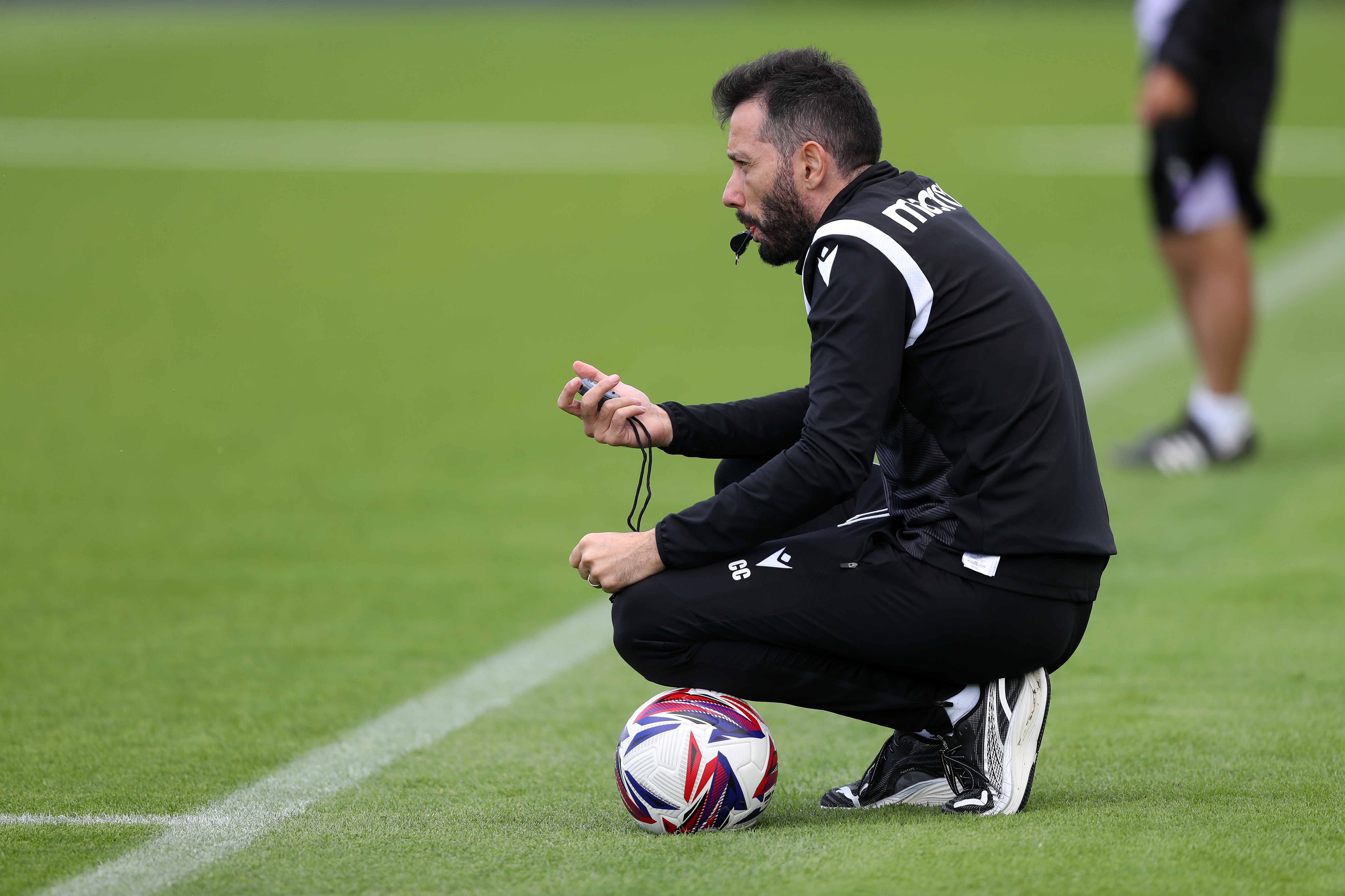 Carlos Corberán watching training crouched down with a whistle and a ball