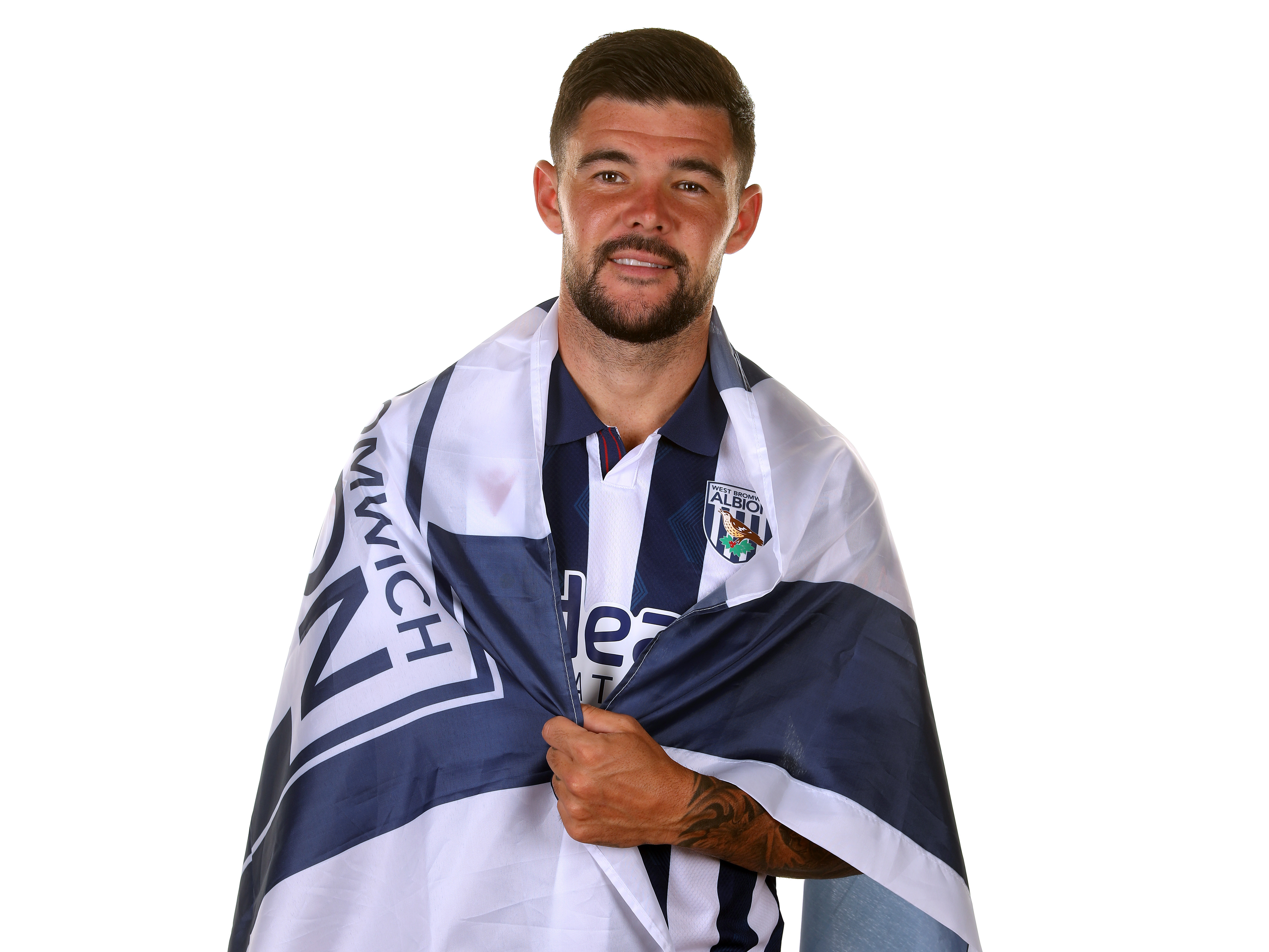 Alex Mowatt looking at the camera while wearing the home shirt and wrapped in a WBA flag