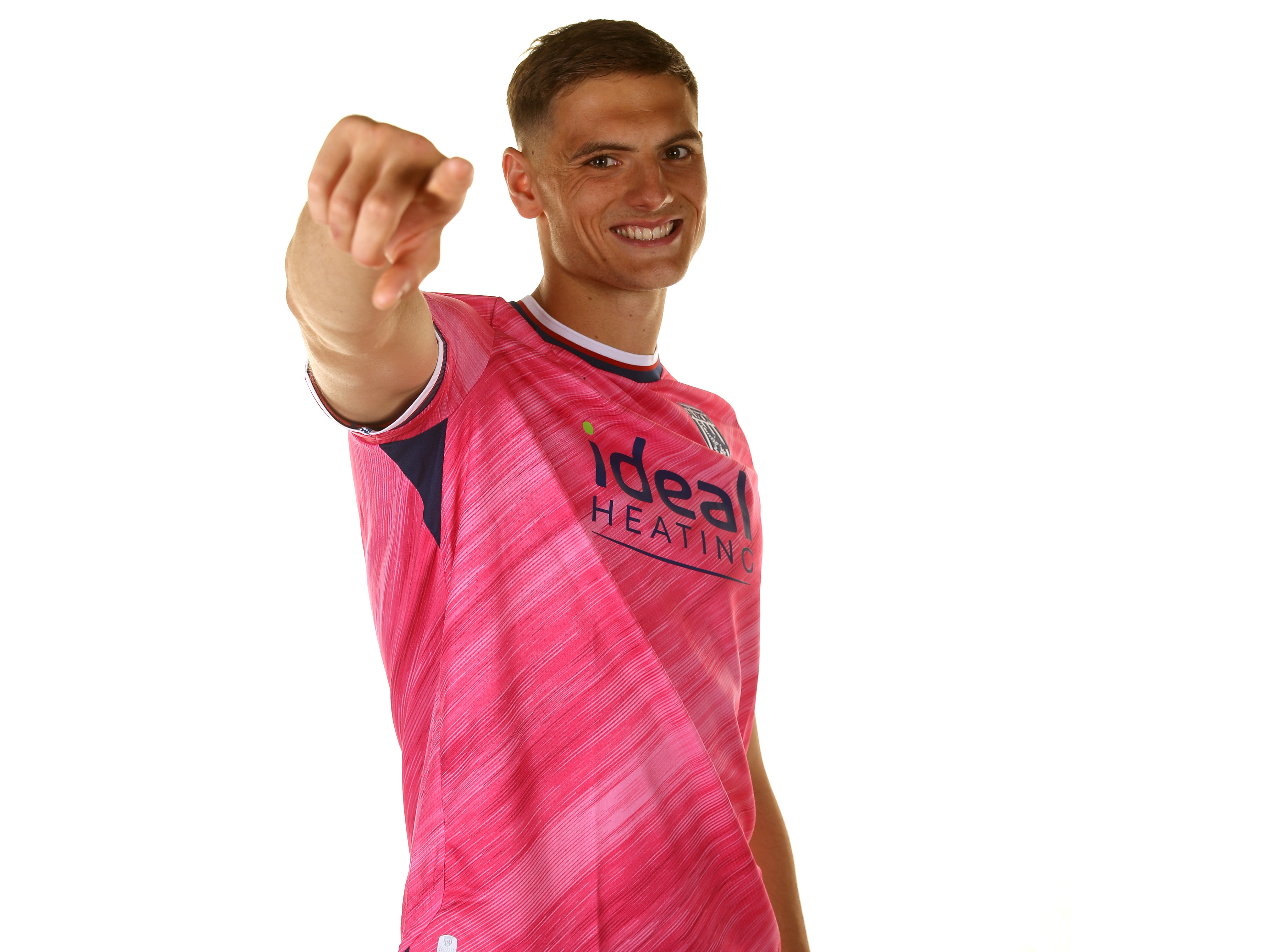 Caleb Taylor pointing at the camera and smiling while wearing the pink away kit 