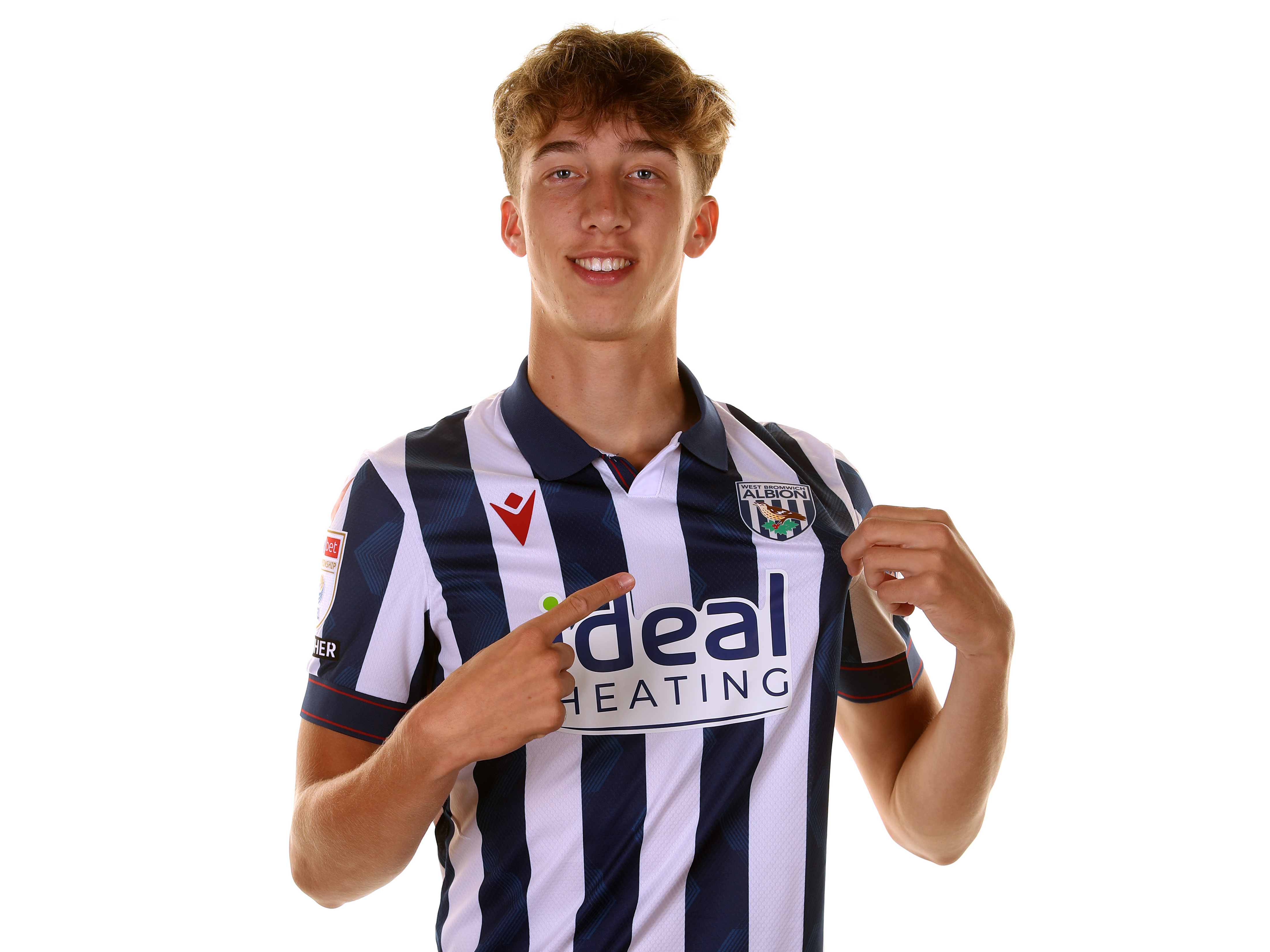 Harry Whitwell pointing to the badge on the home shirt smiling at the camera 