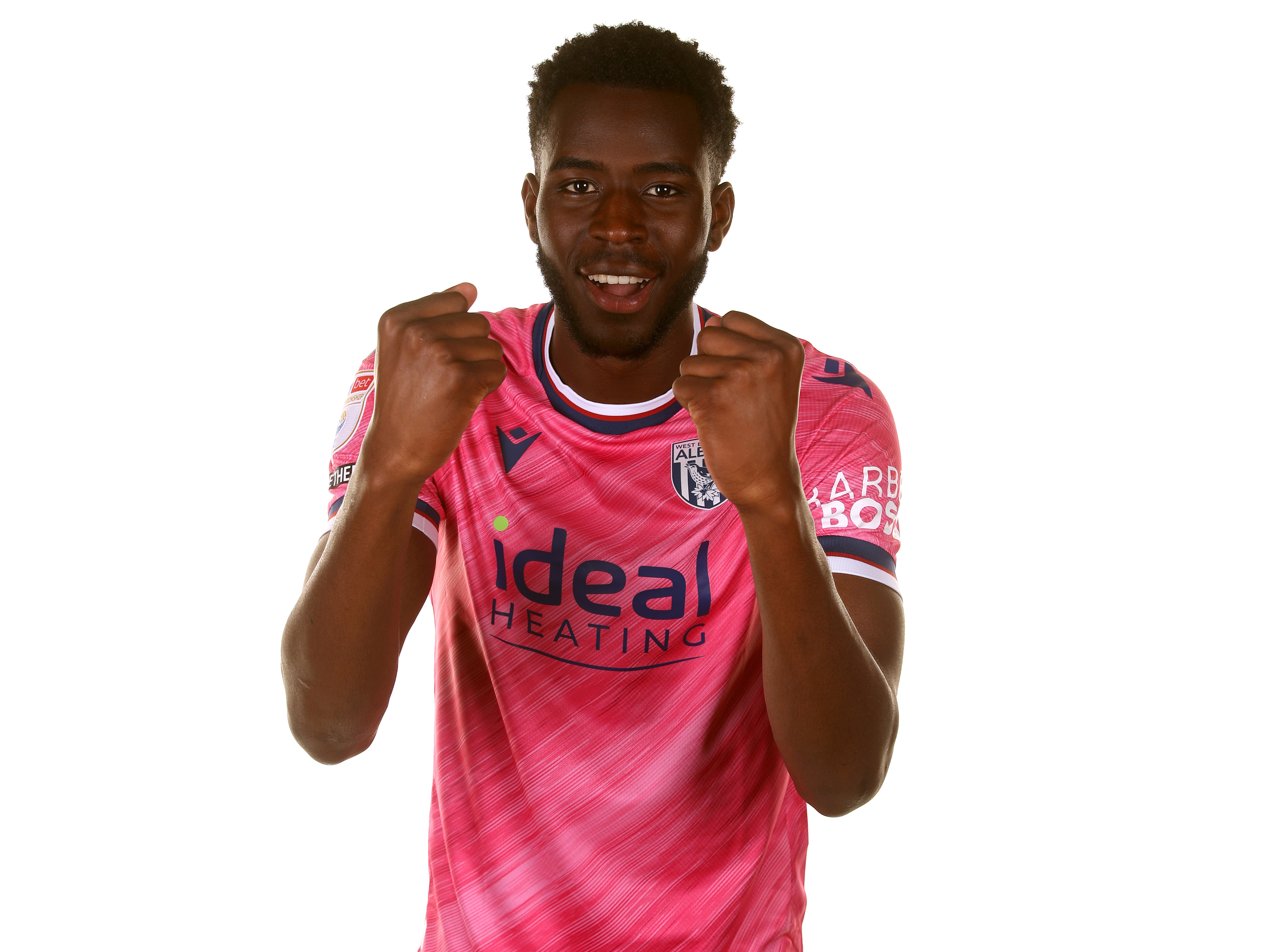 Mo Faal with his fists clenched smiling at the camera while wearing the pink away shirt 