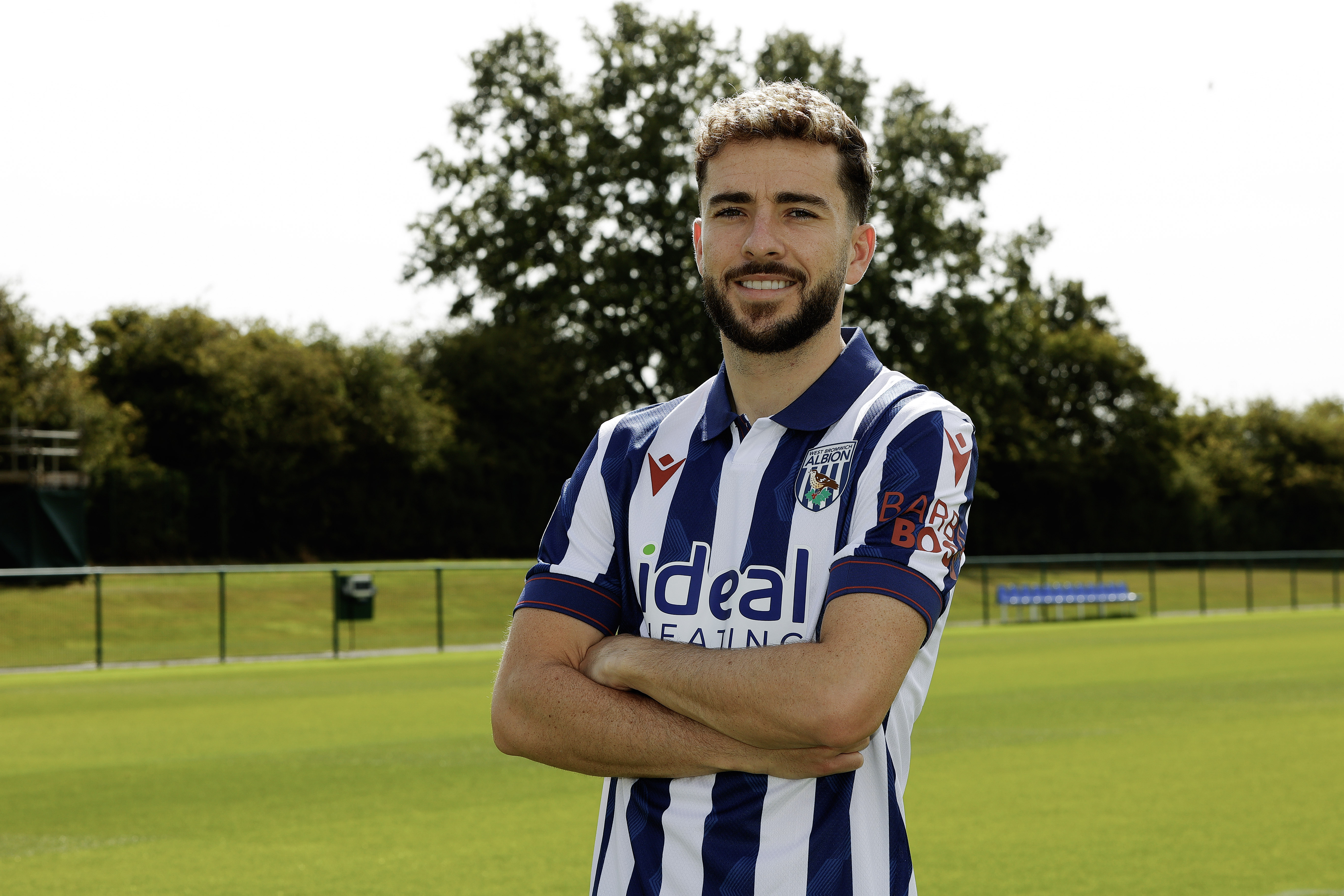 Mikey Johnston smiling at the camera while stood with his arms folded in a home shirt 