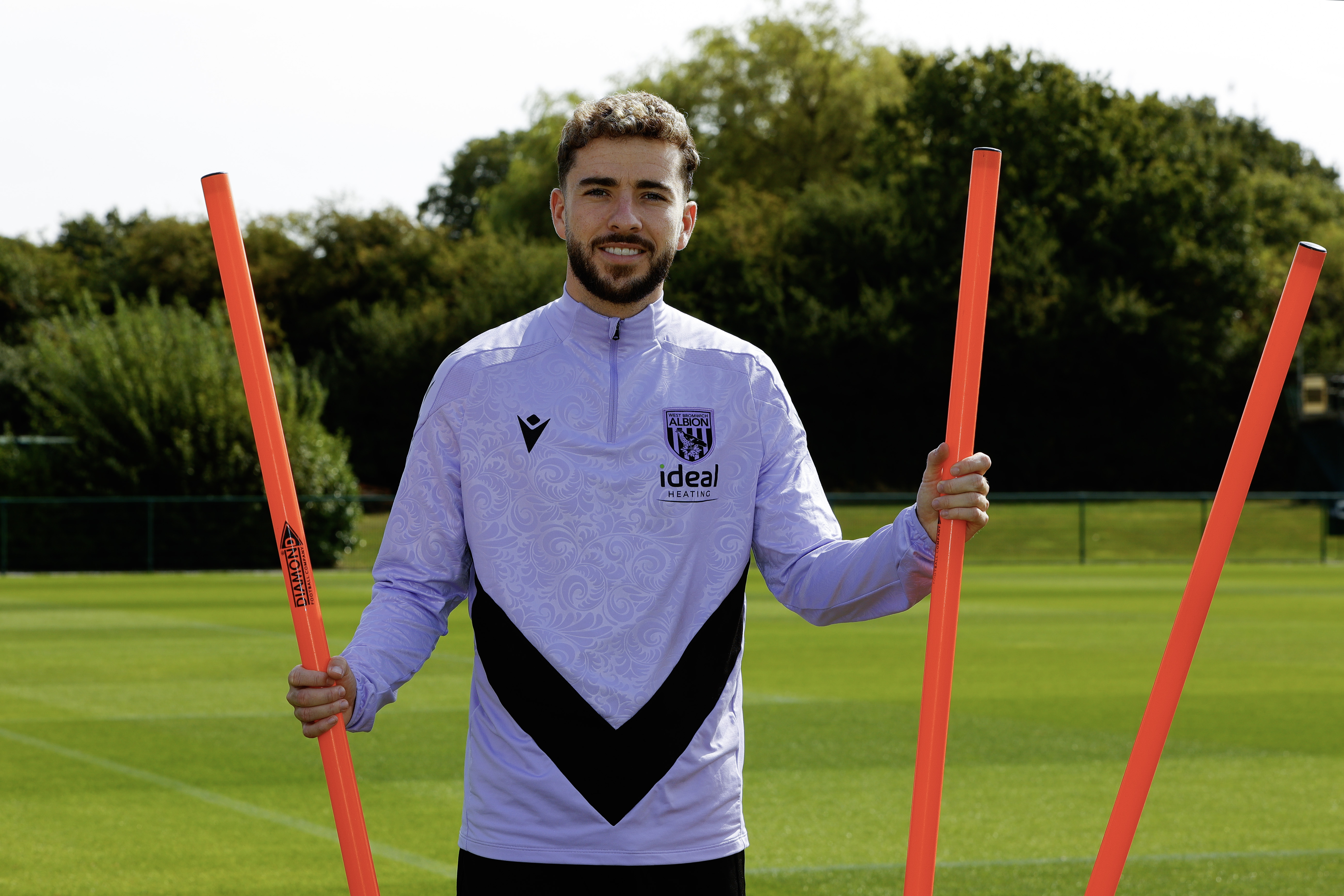 Mikey Johnston smiling at the camera while stood by some poles on the training pitch