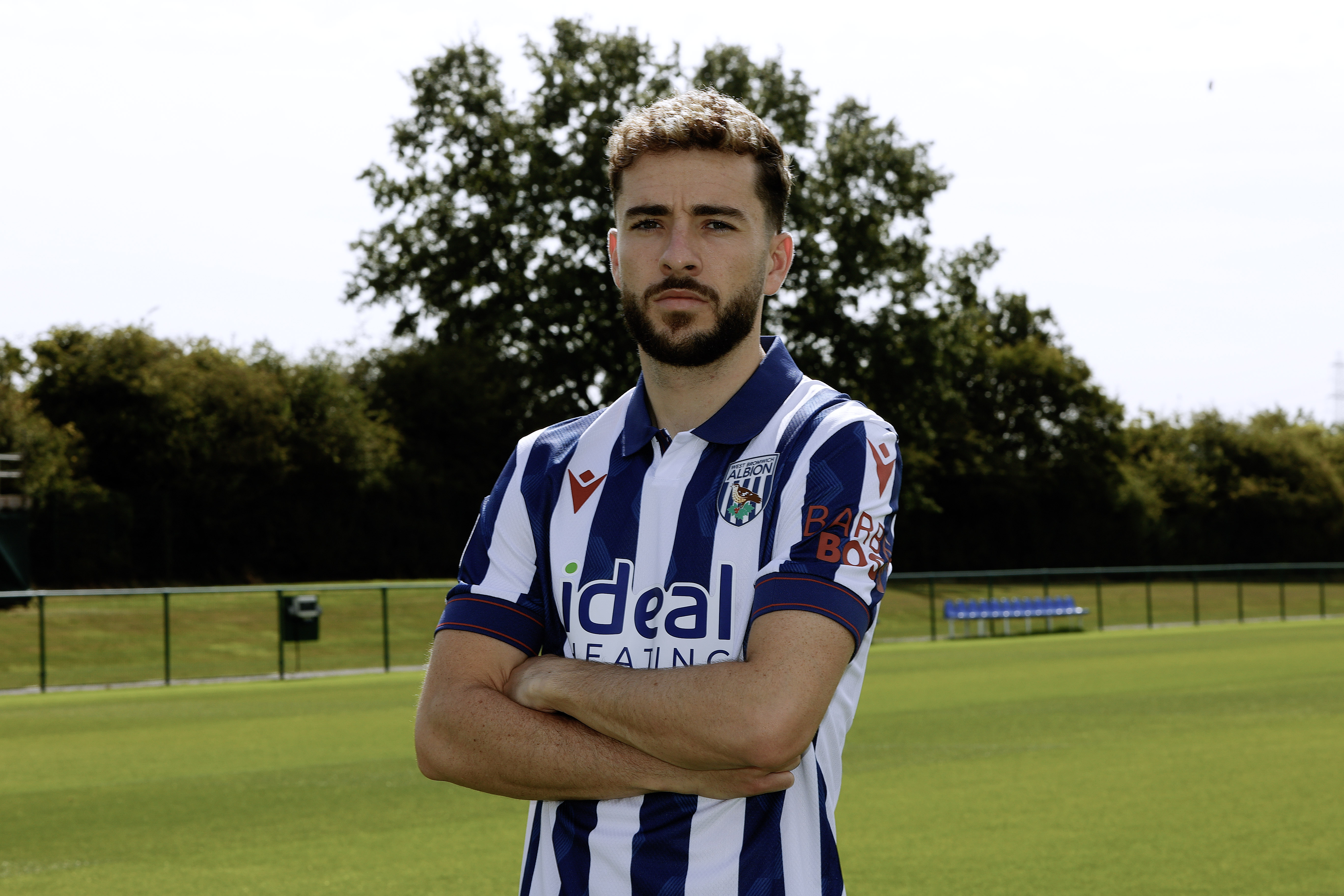 Mikey Johnston looking at the camera while stood with his arms folded in a home shirt 