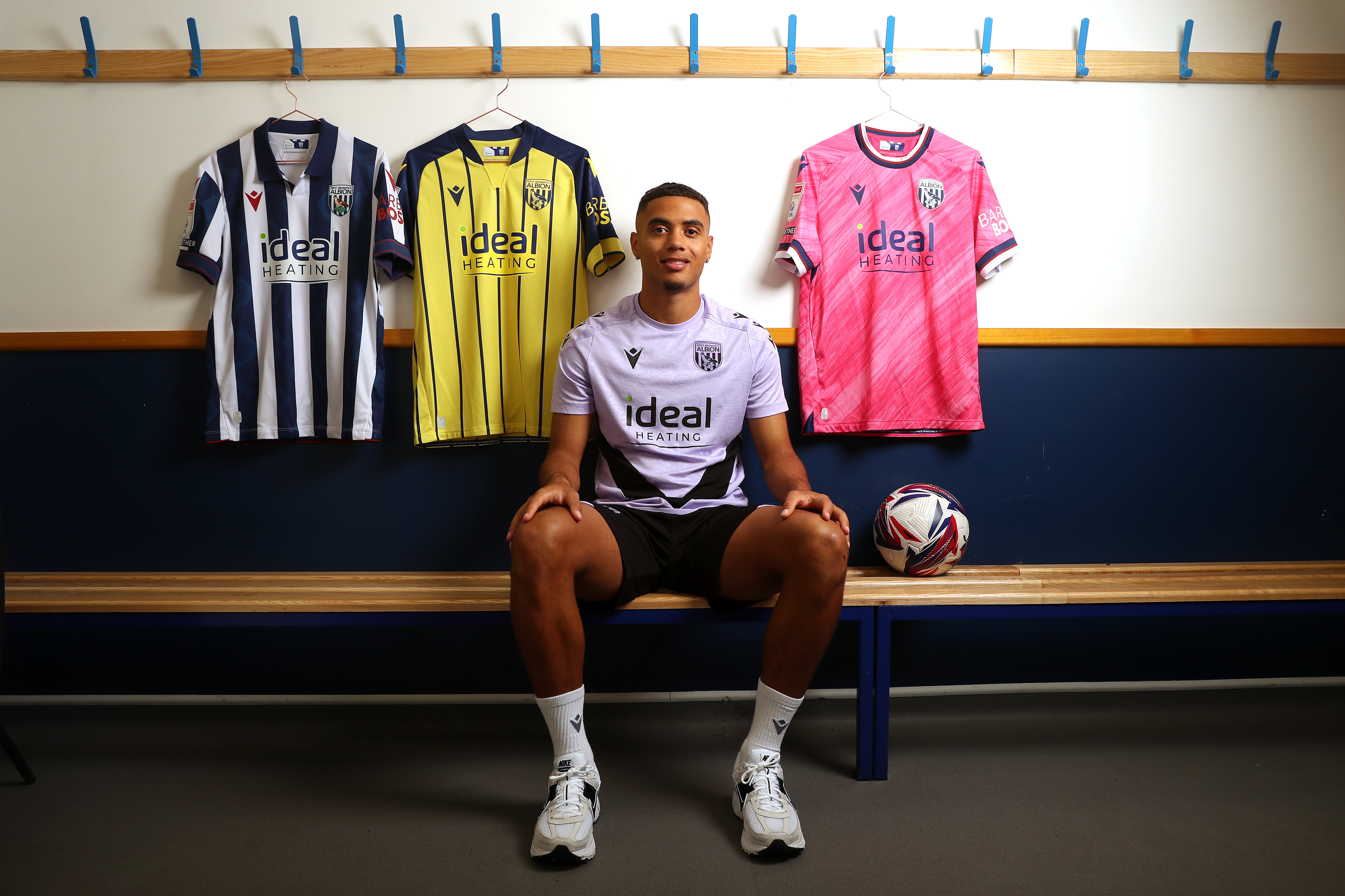 Lewis Dobbin sat in a changing room with the three 2024/25 Albion kits hanging up 