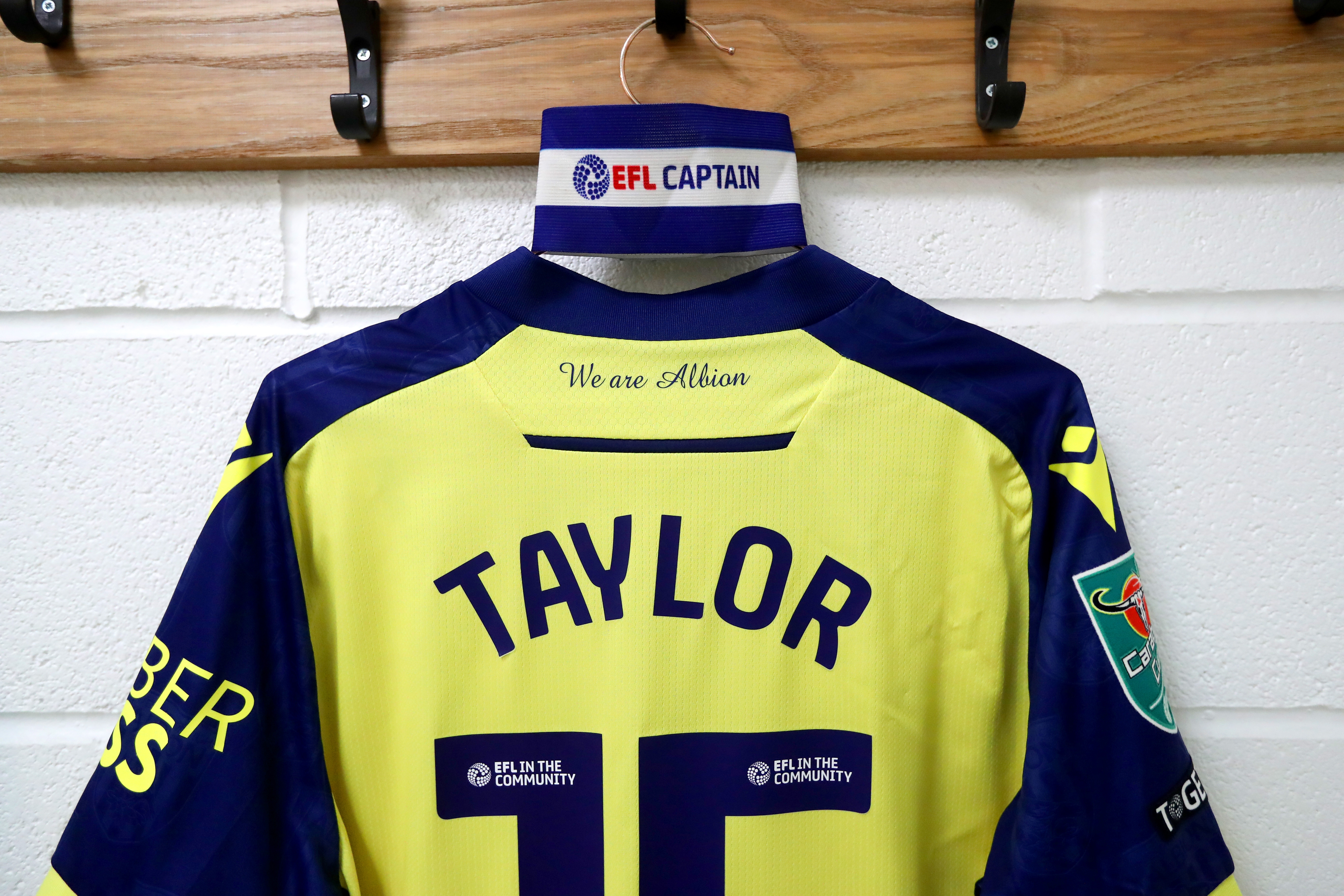 Caleb Taylor's yellow away shirt hanging up in the dressing room at Fleetwood with the captain's armband on the peg 