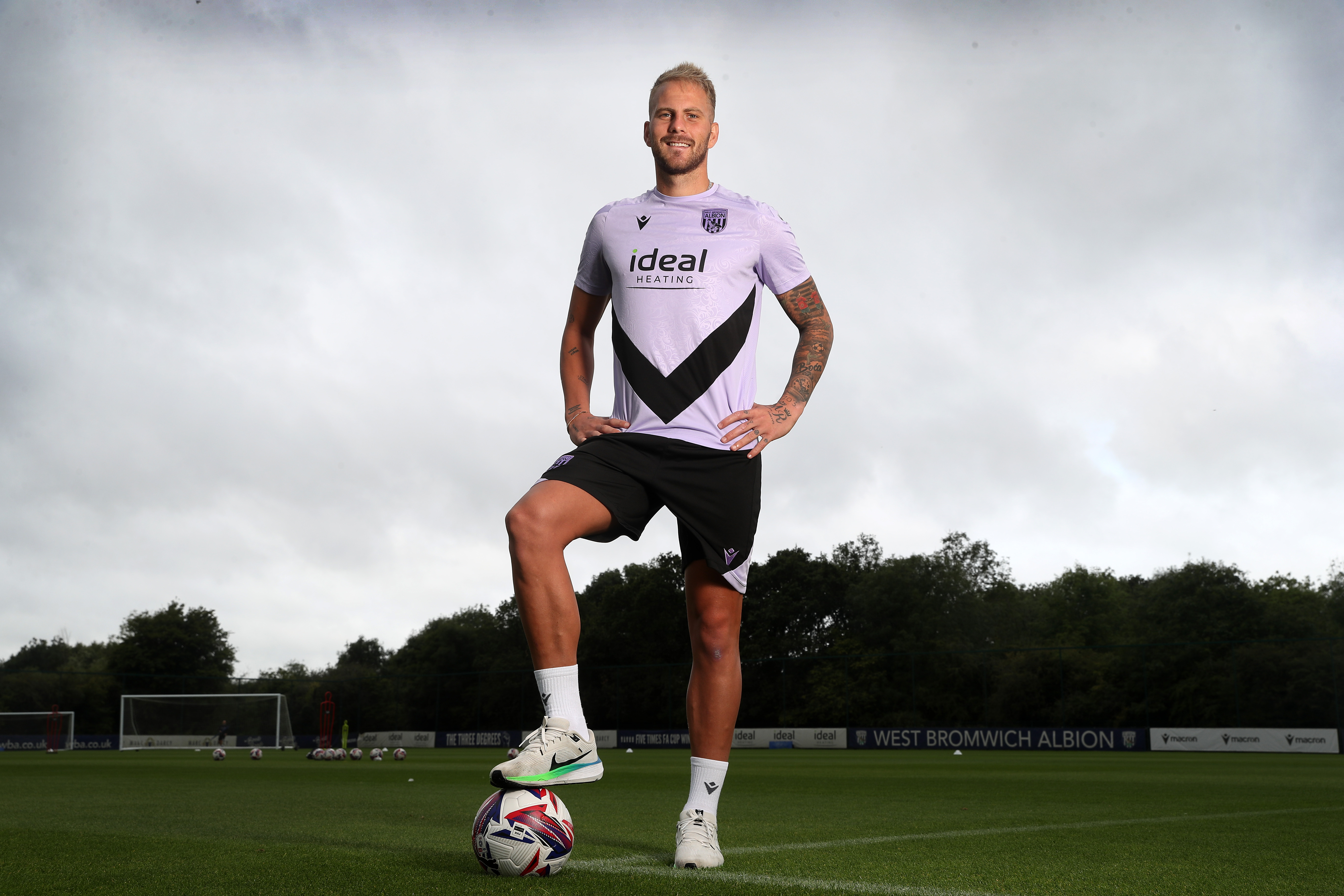 Uroš Račić stood on a training pitch with his foot on the ball and hands on his hips smiling at the camera  