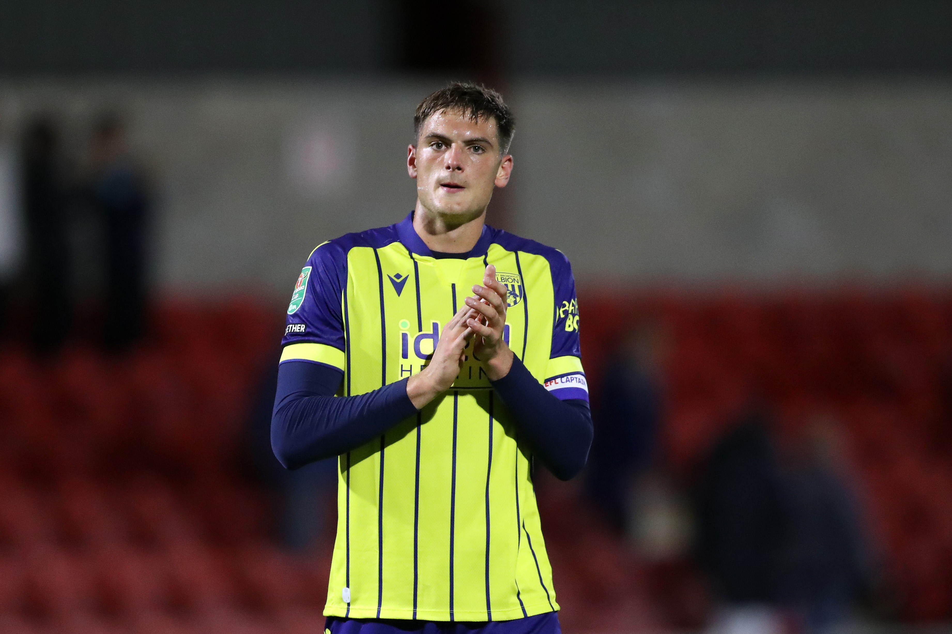 Caleb Taylor applauds Albion fans at Fleewood while wearing the yellow away kit 