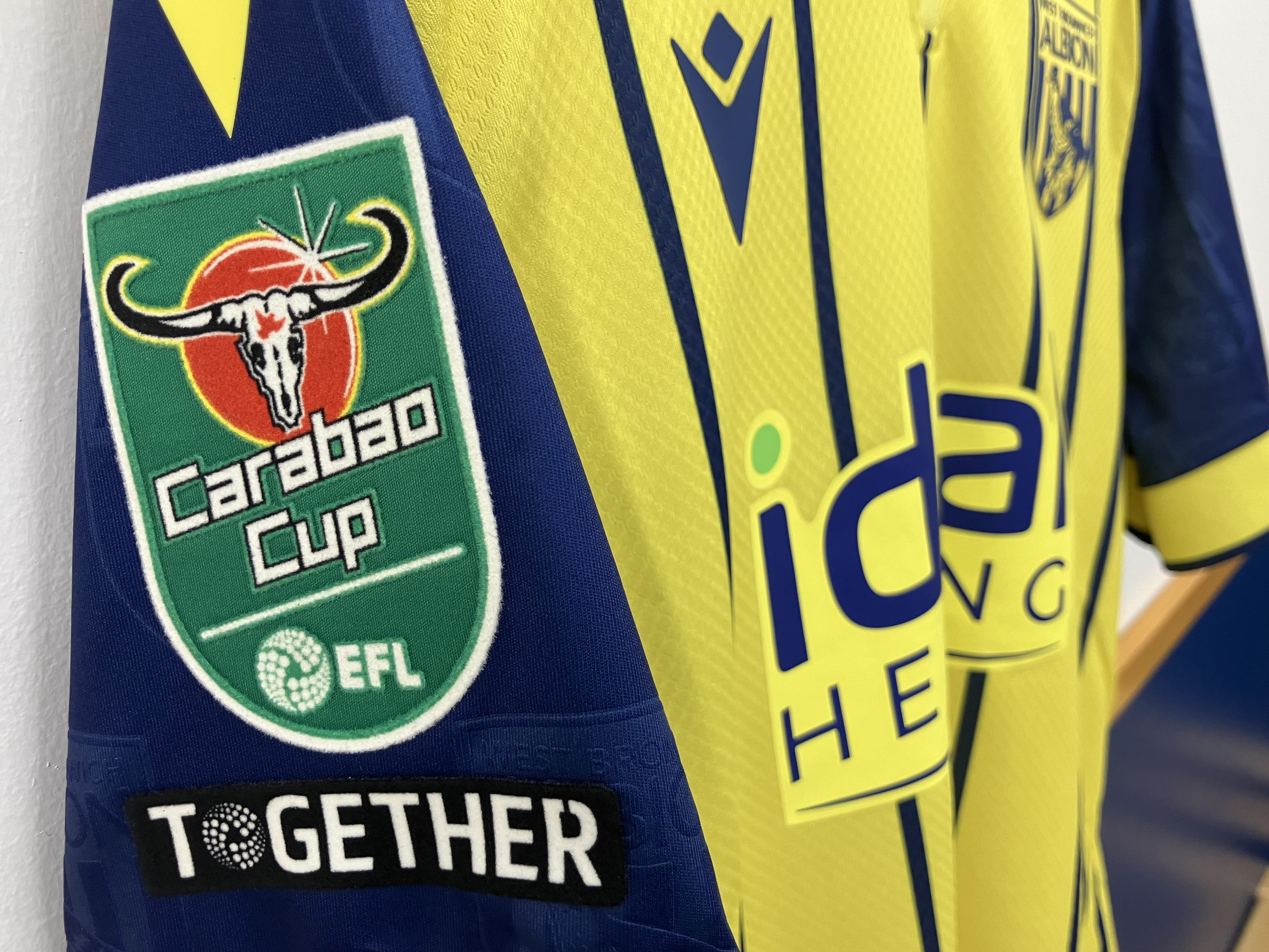 An image of a yellow away kit hanging in dressing room with the Carabao Cup badge on