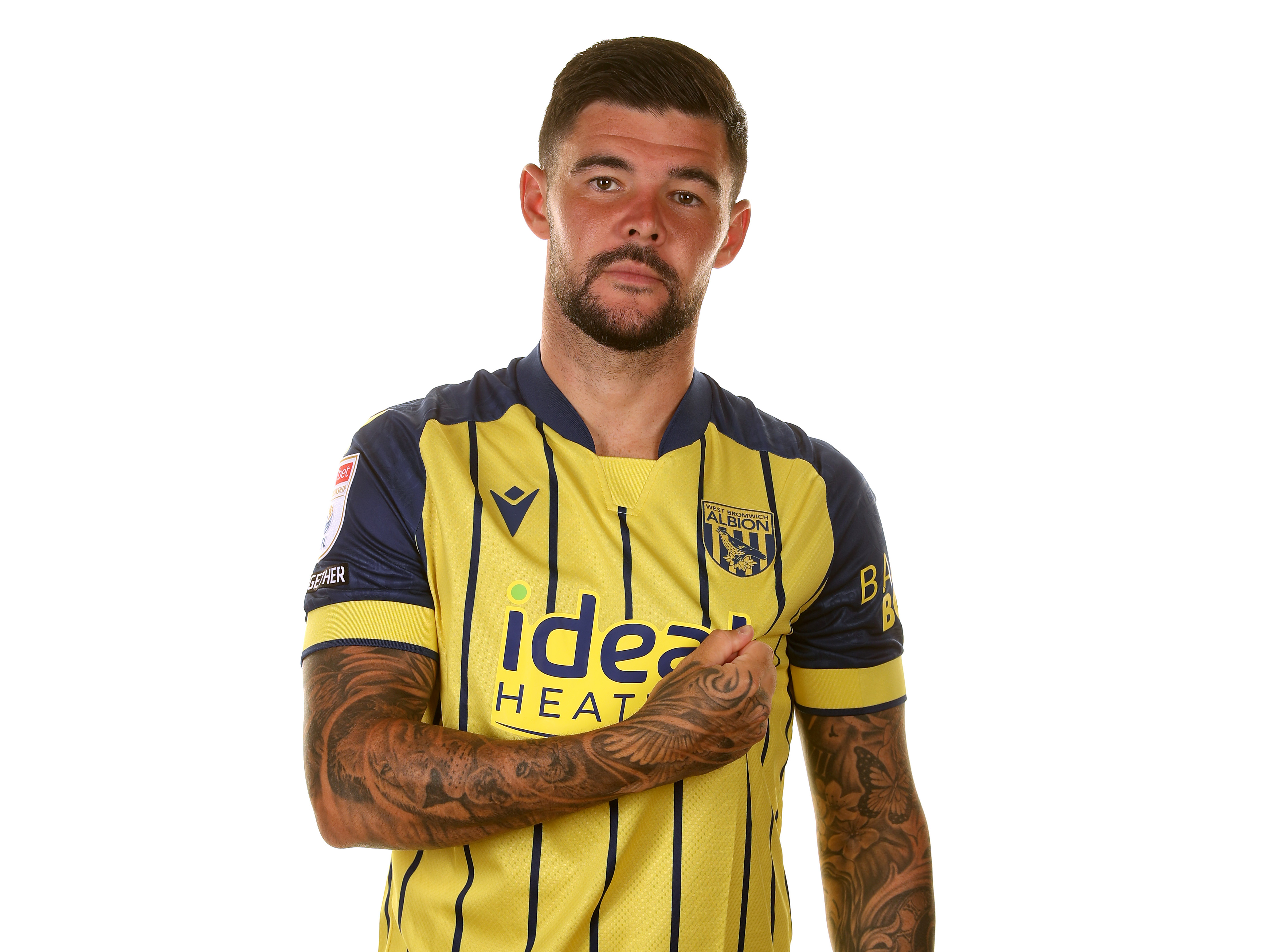 Alex Mowatt looking at the camera while in the yellow away shirt pulling on the badge 