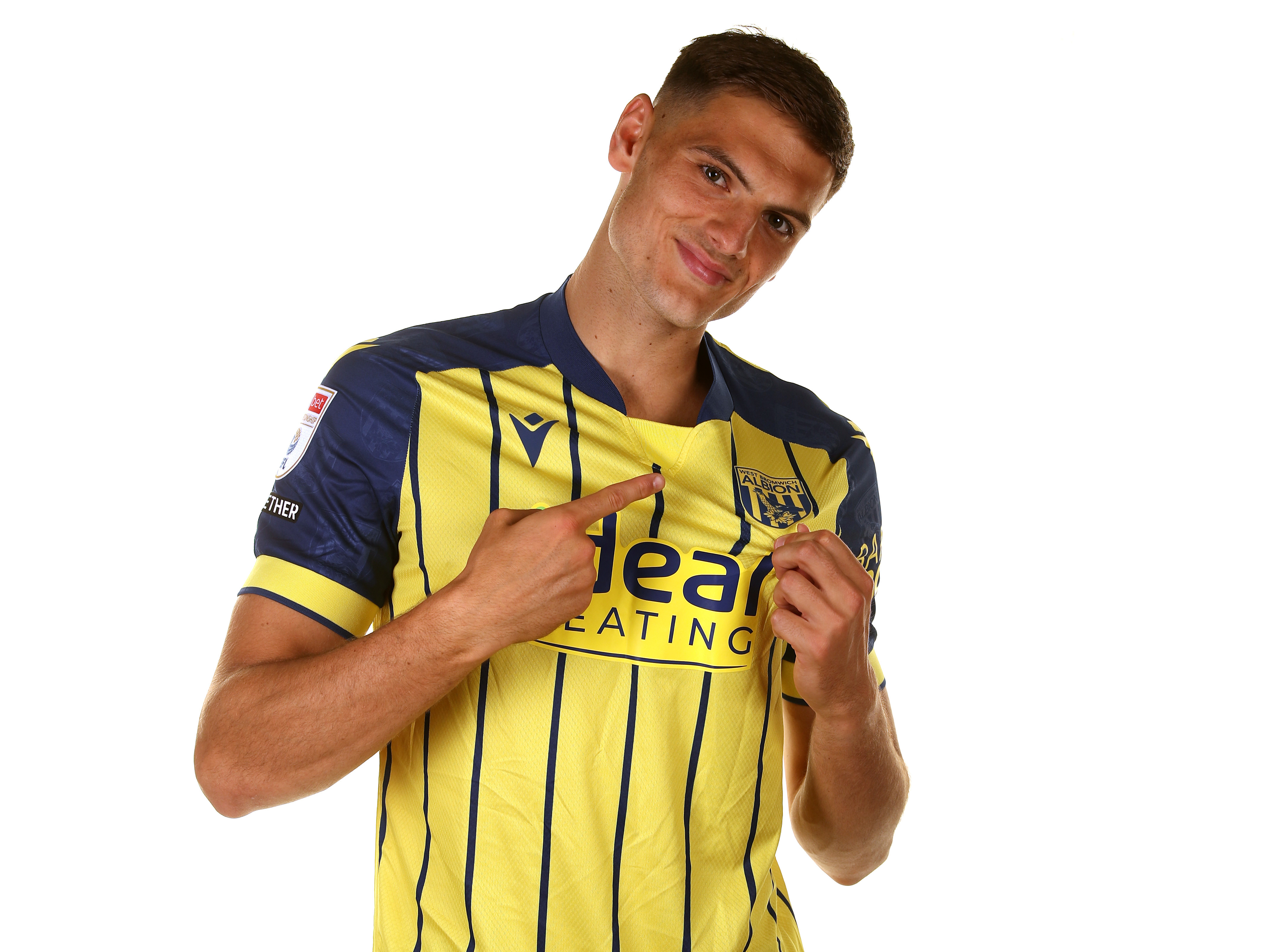 Caleb Taylor pointing to the badge on the yellow away shirt 