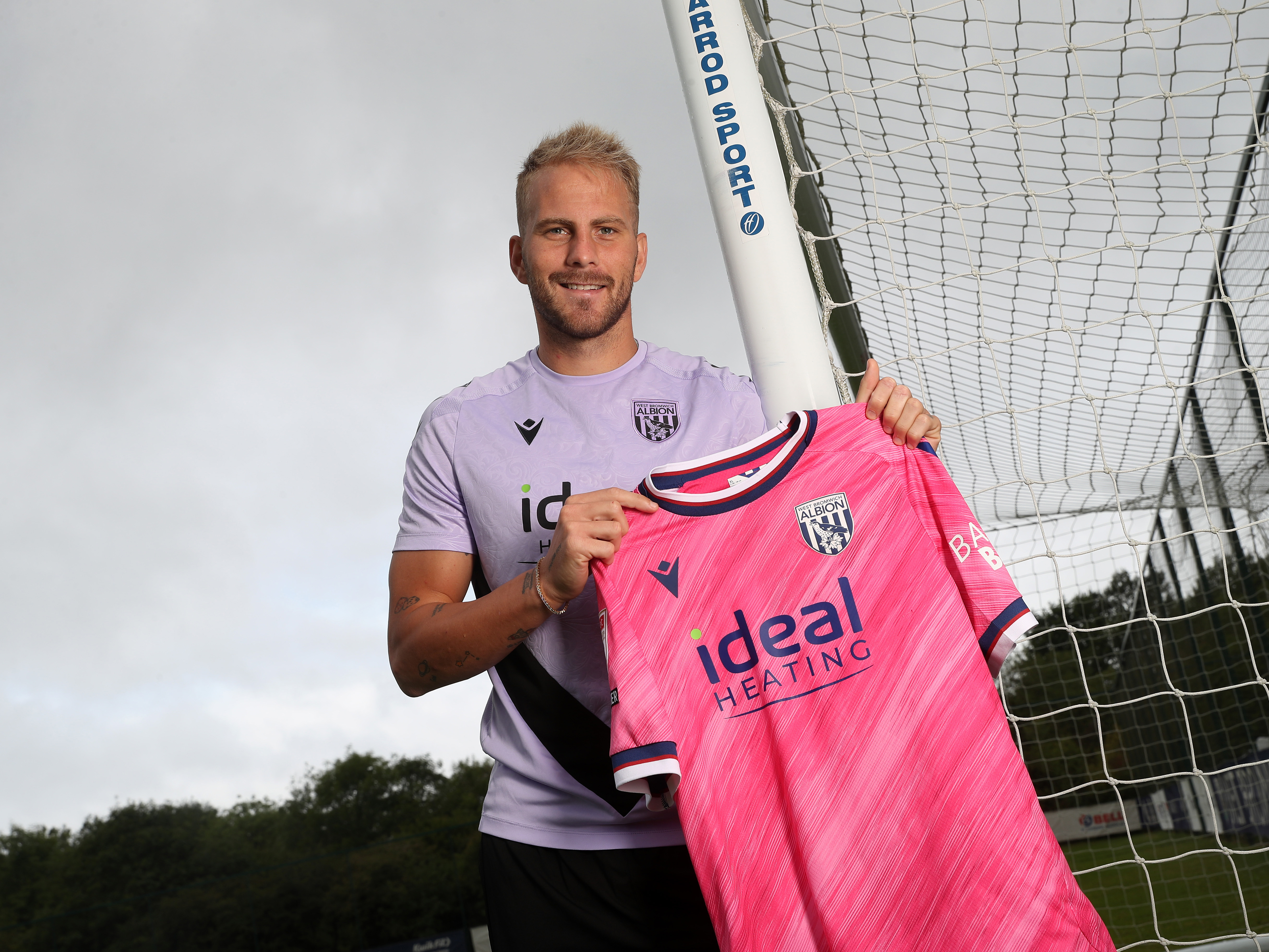 Uroš Račić smiling at the camera while holding up a pink away shirt 